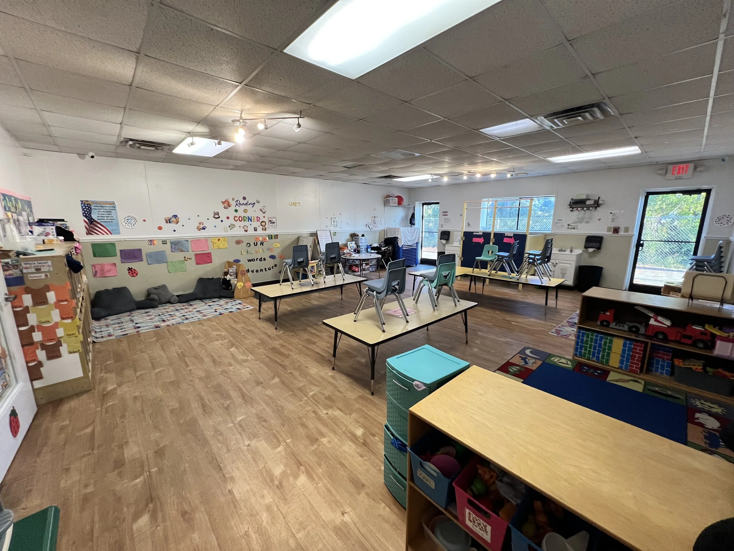 Classroom with tables and chairs, educational decorations on the walls, and sunlight coming through windows.