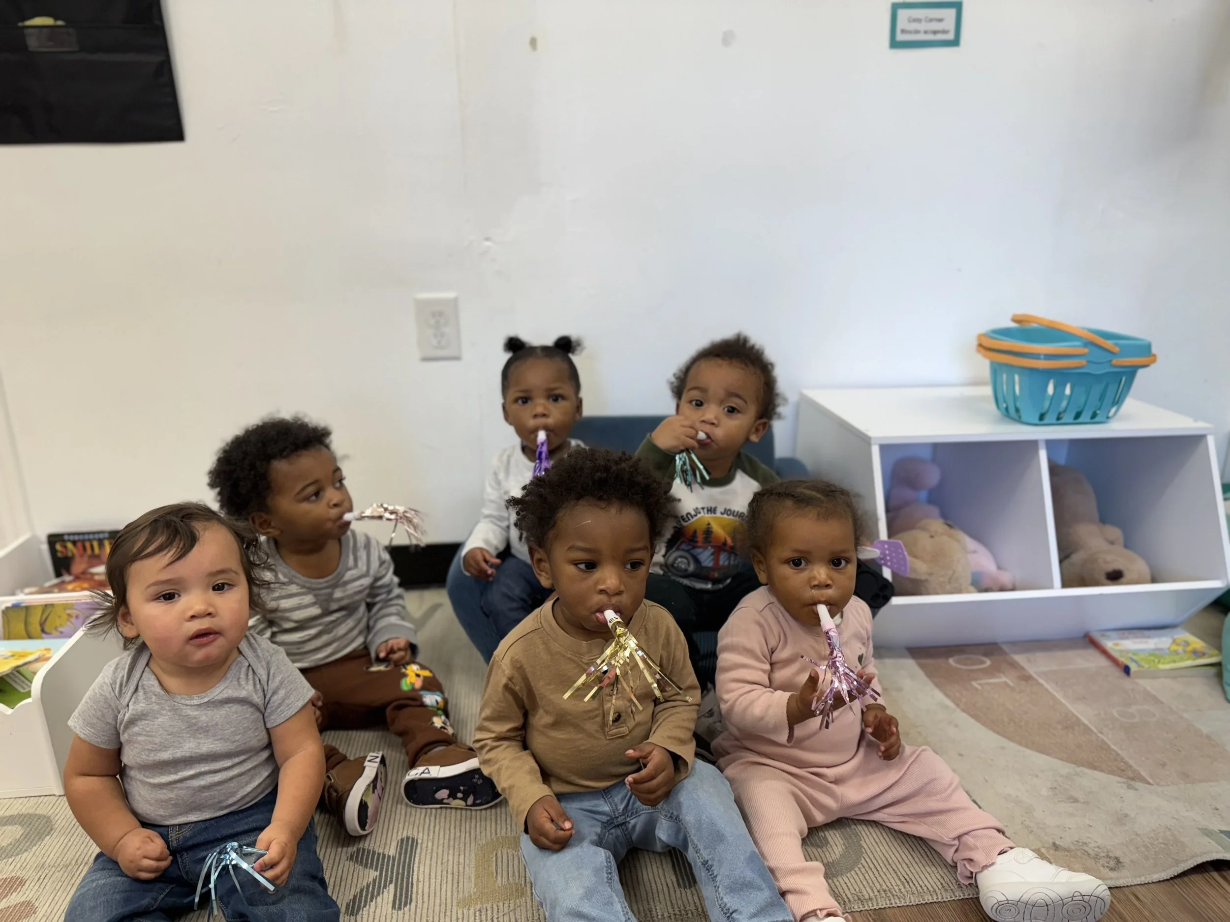 Group of young children sitting on the floor at a party, some holding party hats and others eating snacks