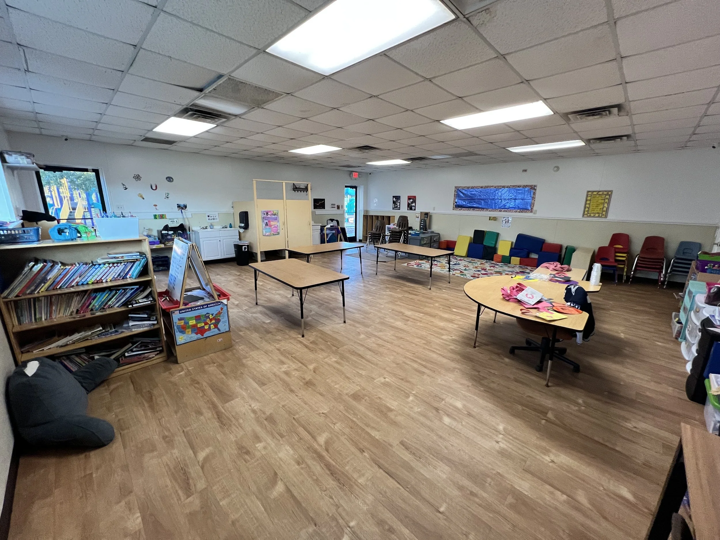 A classroom with a wooden floor, tables, chairs, books, and educational materials.