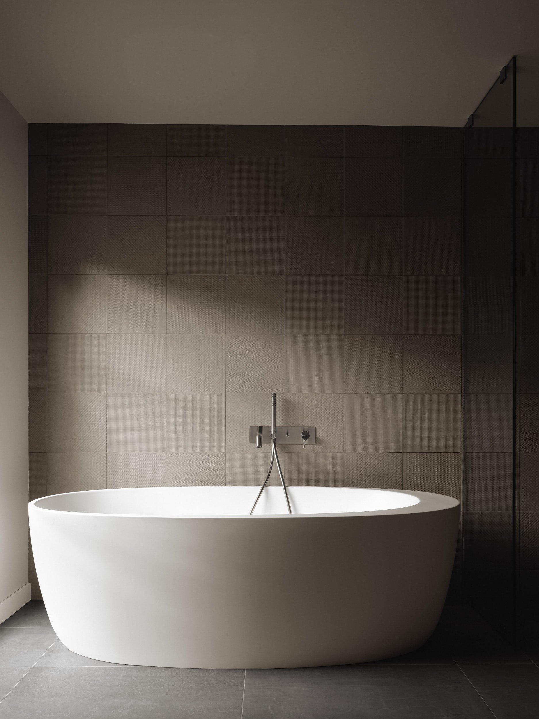Baignoire blanc dans une salle de bain moderne avec mur en carreaux gris foncé et sol en carrelage gris clair, vue frontale