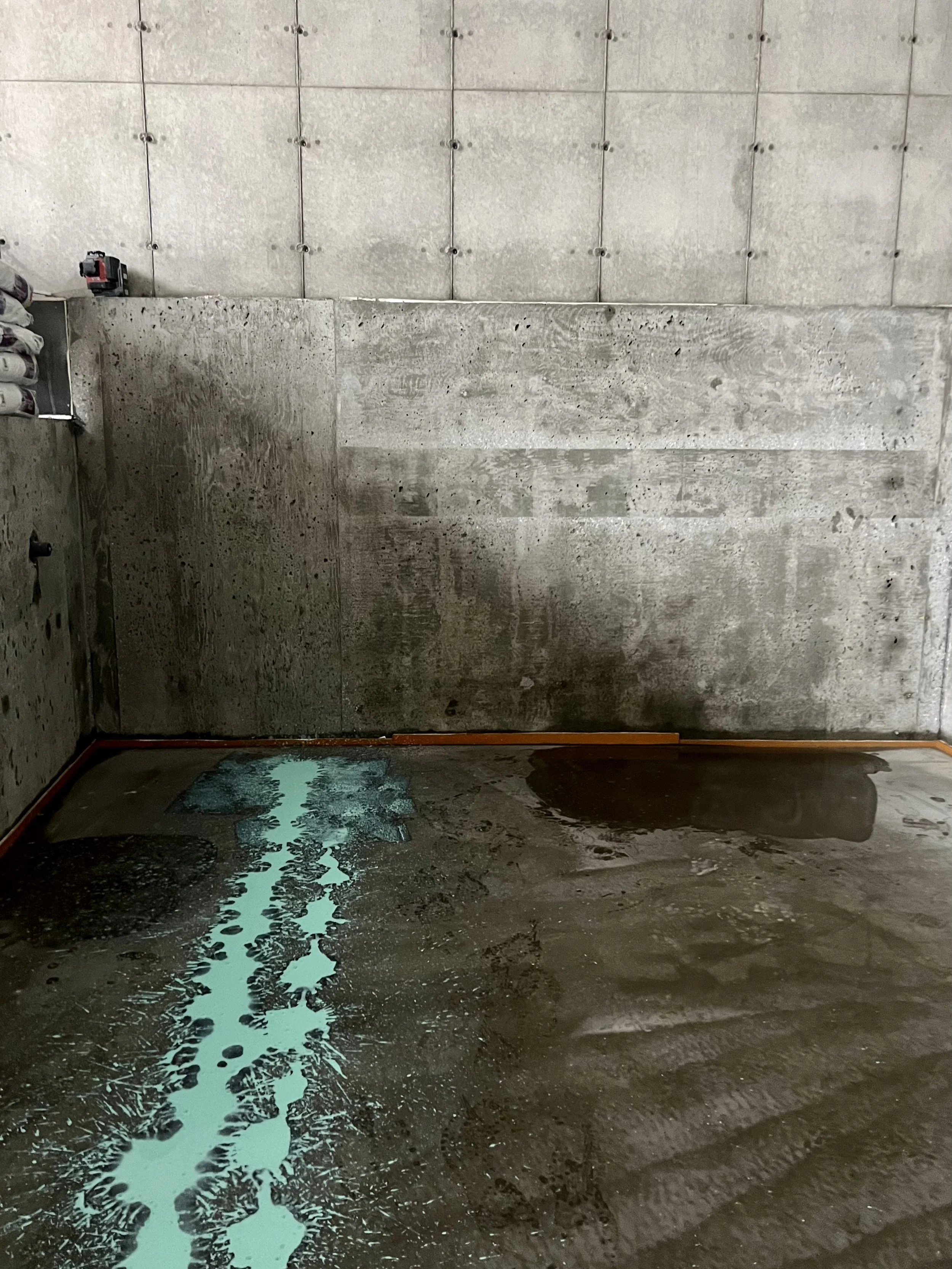 Sol en béton en construction avec une flaque d'eau turquoise et un mur en céramique.