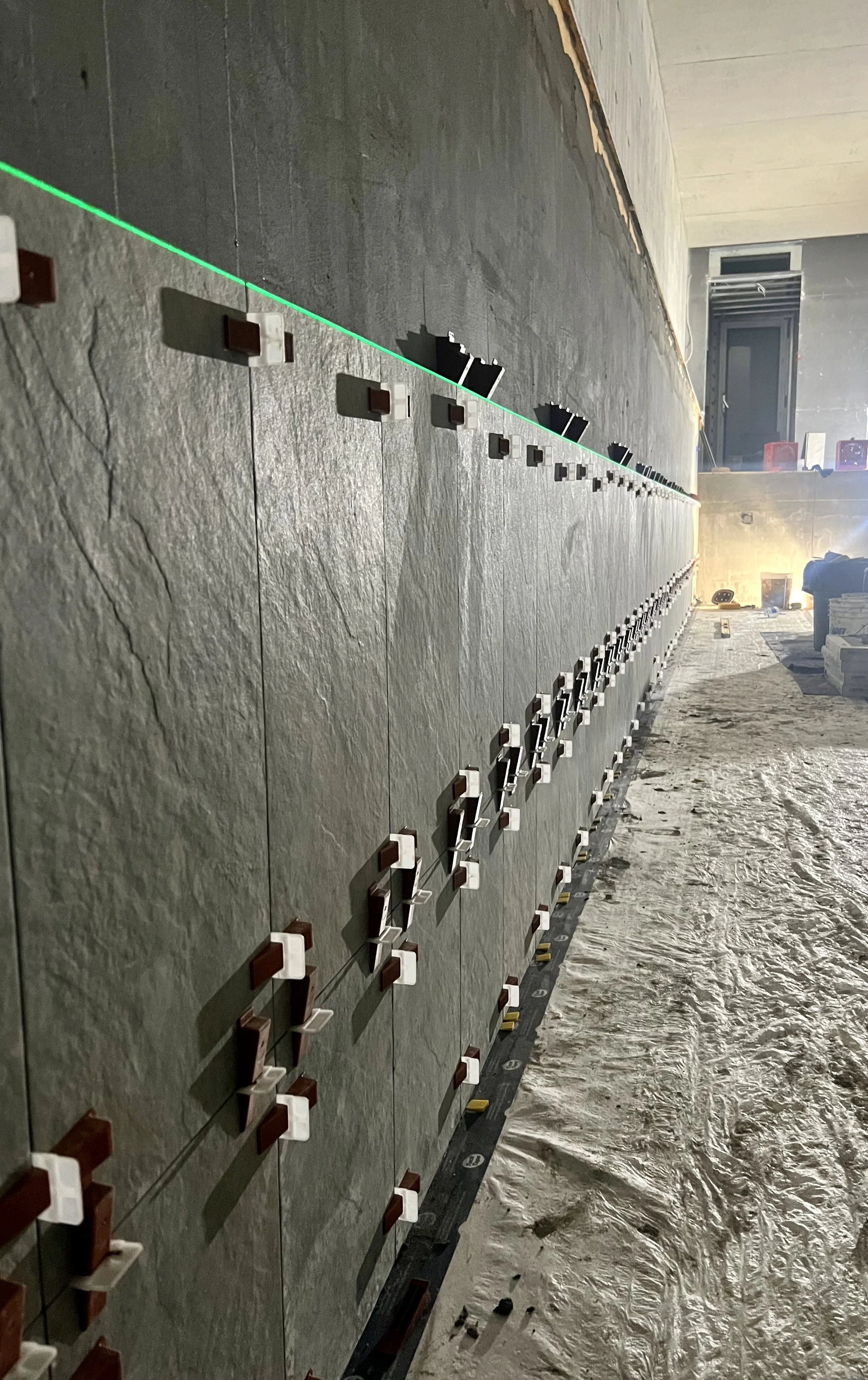 Installation en cours de carreaux de pierre sur un mur intérieur, avec un niveau laser vert pour assurer l'alignement précis.