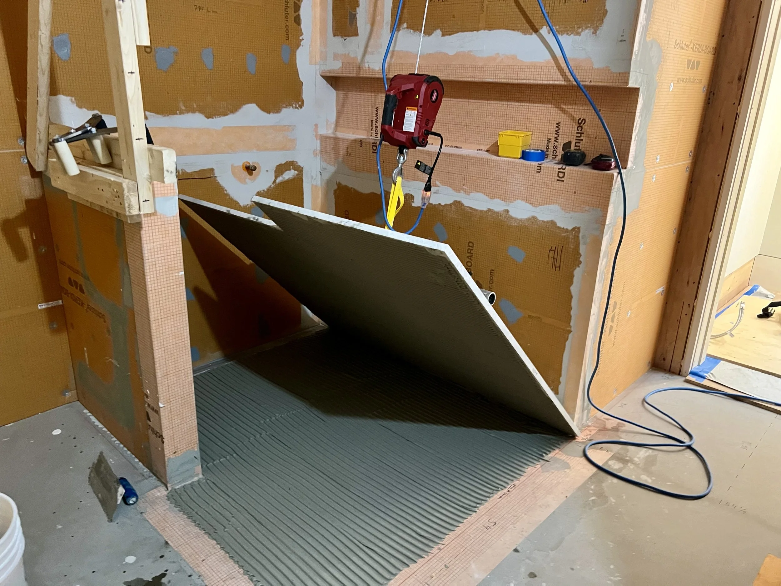 Travaux en cours dans une pièce, murs en travaux avec isolation et câblage électriques visibles, outils et matériaux de construction présents, sol en travaux avec un tapis ou revêtement temporaire.