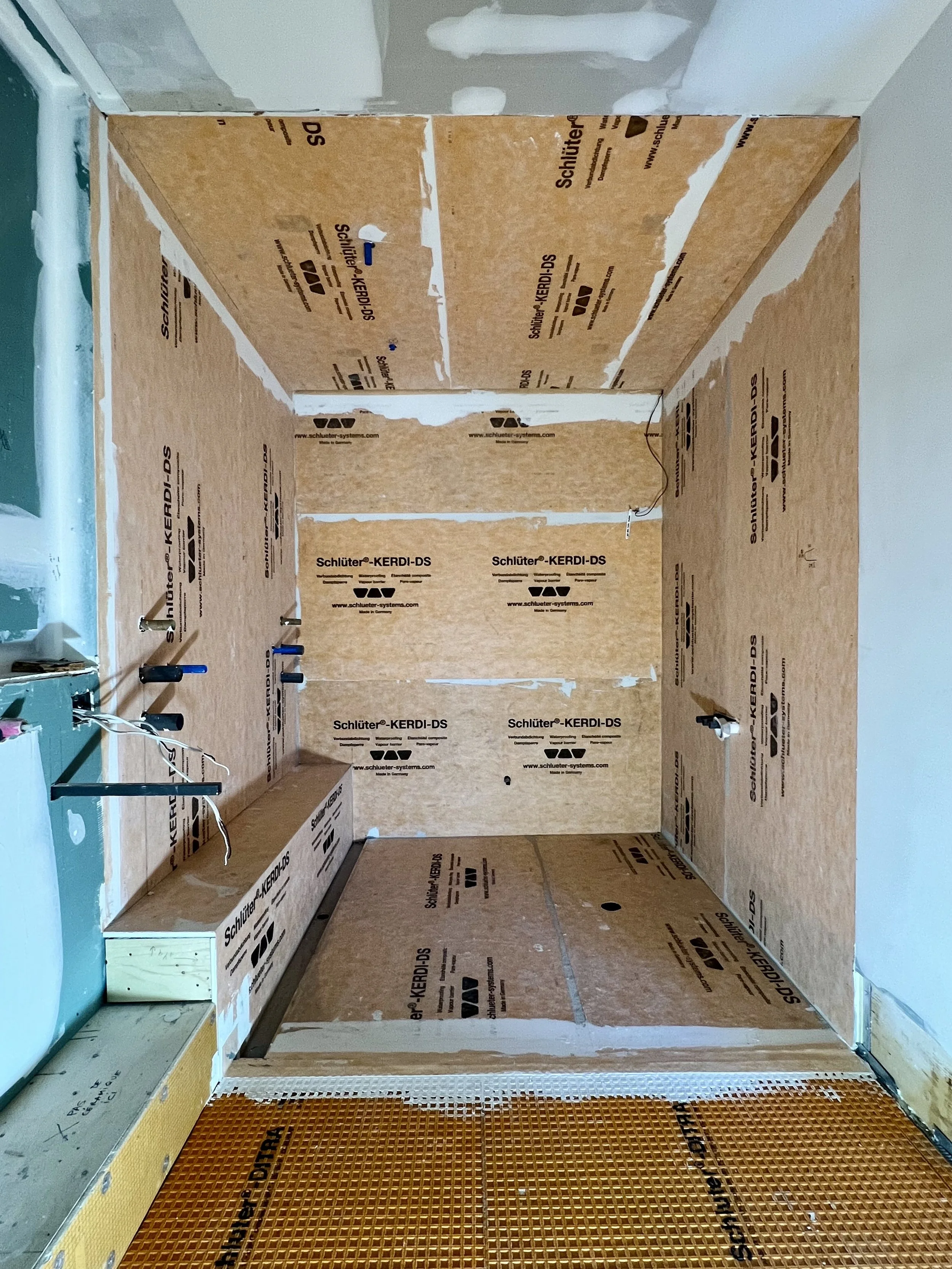 Une pièce en cours de construction ou de rénovation avec des murs en bois, des câbles électriques visibles et un sol en grille en plastique orange.