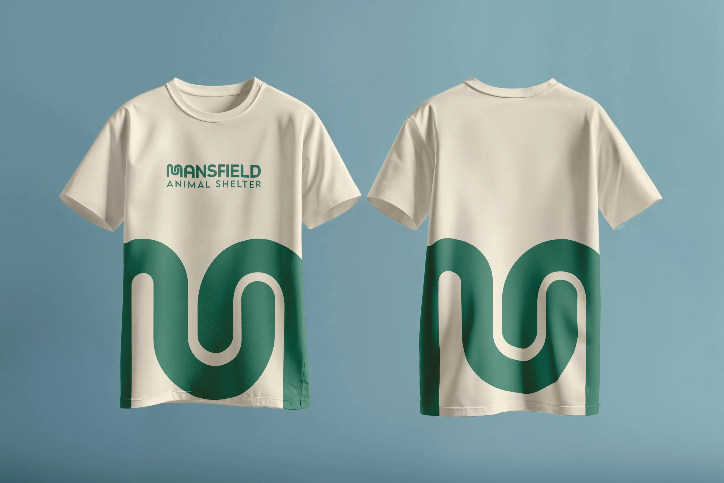Two white T-shirts hanging side by side against a blue background. The left T-shirt has green text that reads 'MANSFIELD ANIMAL SHELTER', and both shirts feature large green and white abstract designs resembling stylized animal shapes or ears.