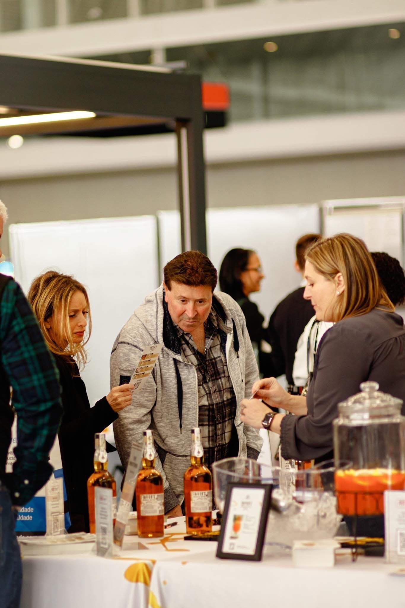People gathered around a table at an event, with bottles of alcohol in the foreground and informational displays on the table.