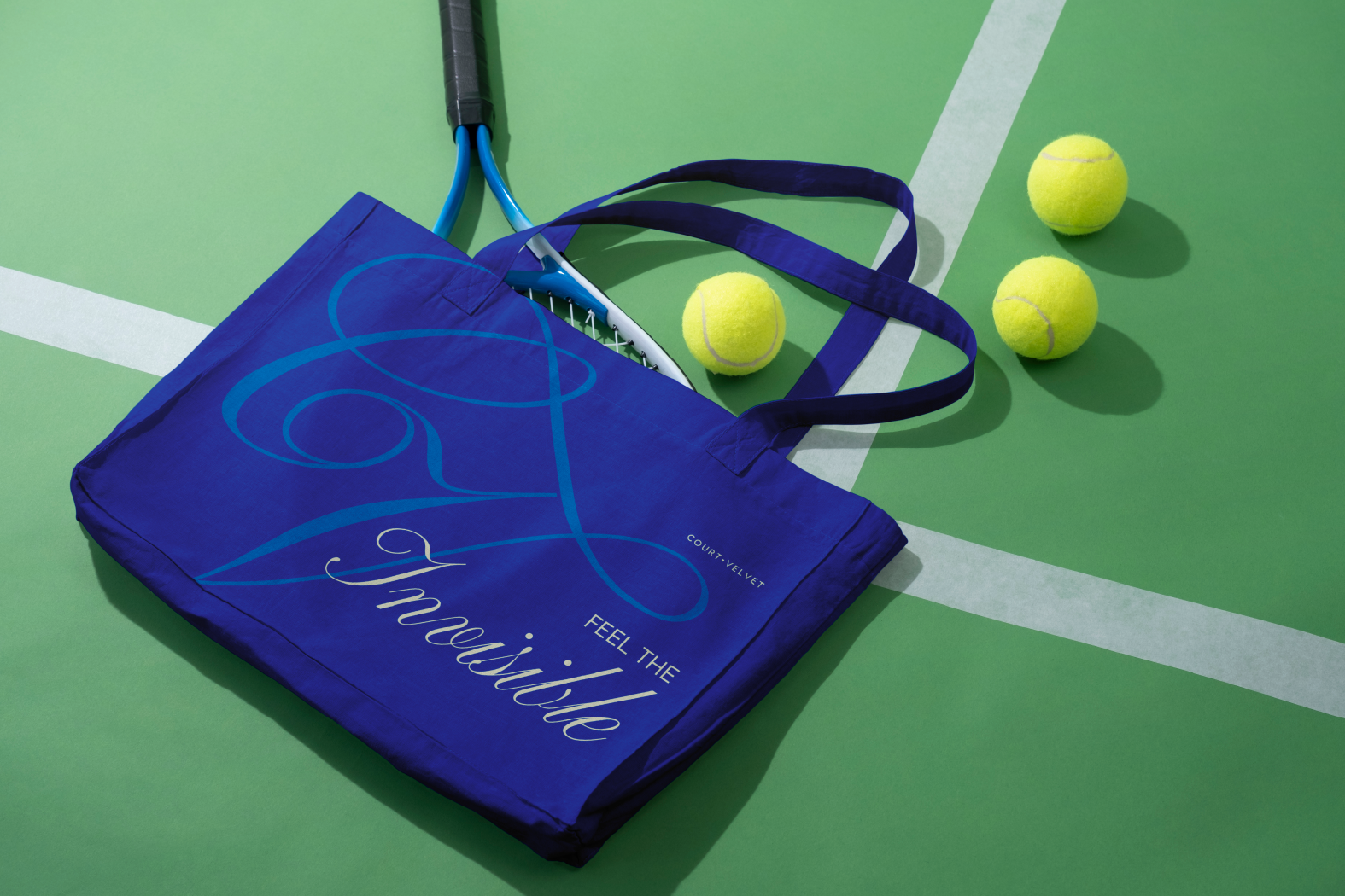 A blue tote bag with tennis-themed design, a tennis racket handle sticking out, and three tennis balls on a green tennis court