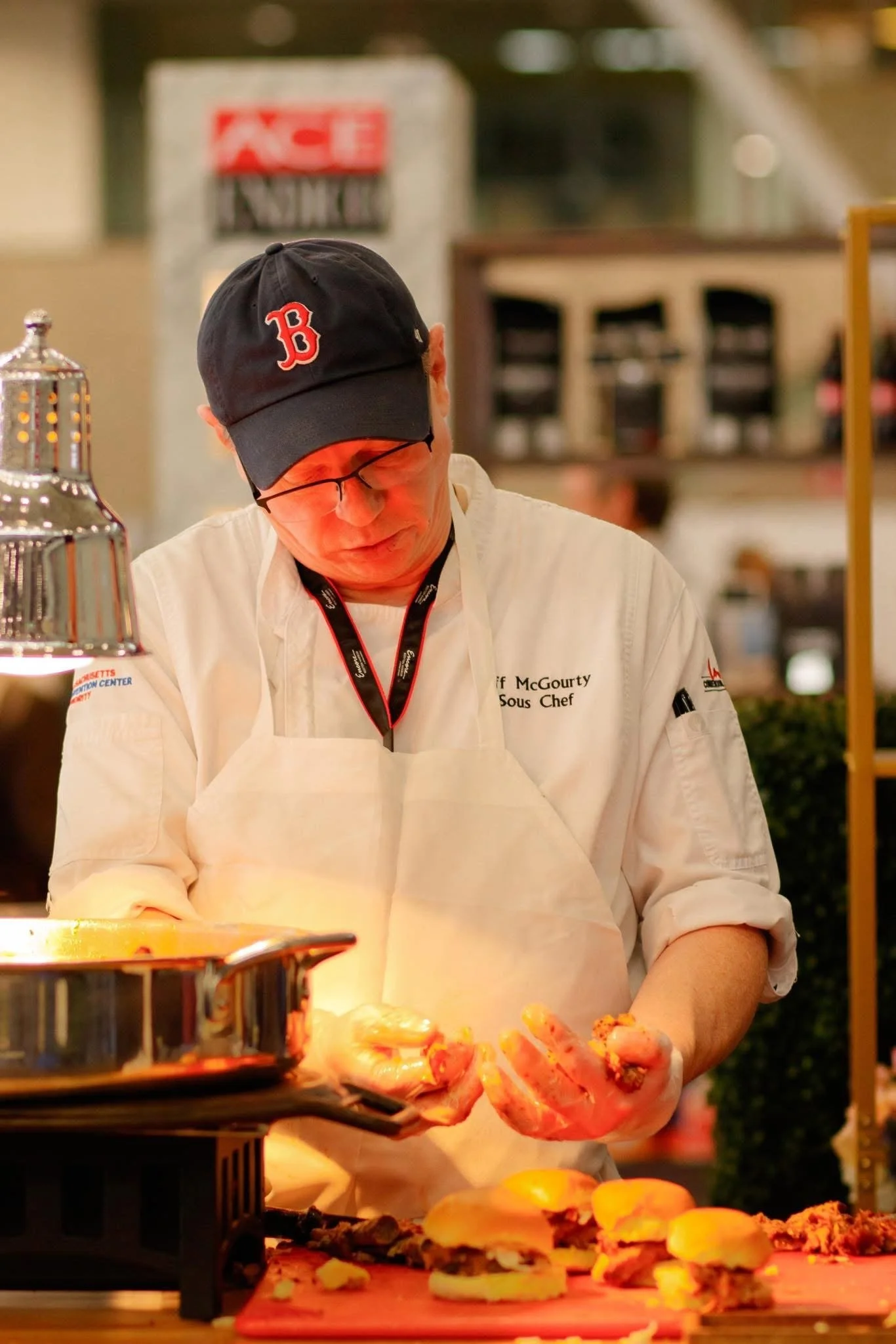 Chef in white uniform and black cap with a red 'B' preparing food at a buffet or catering event.