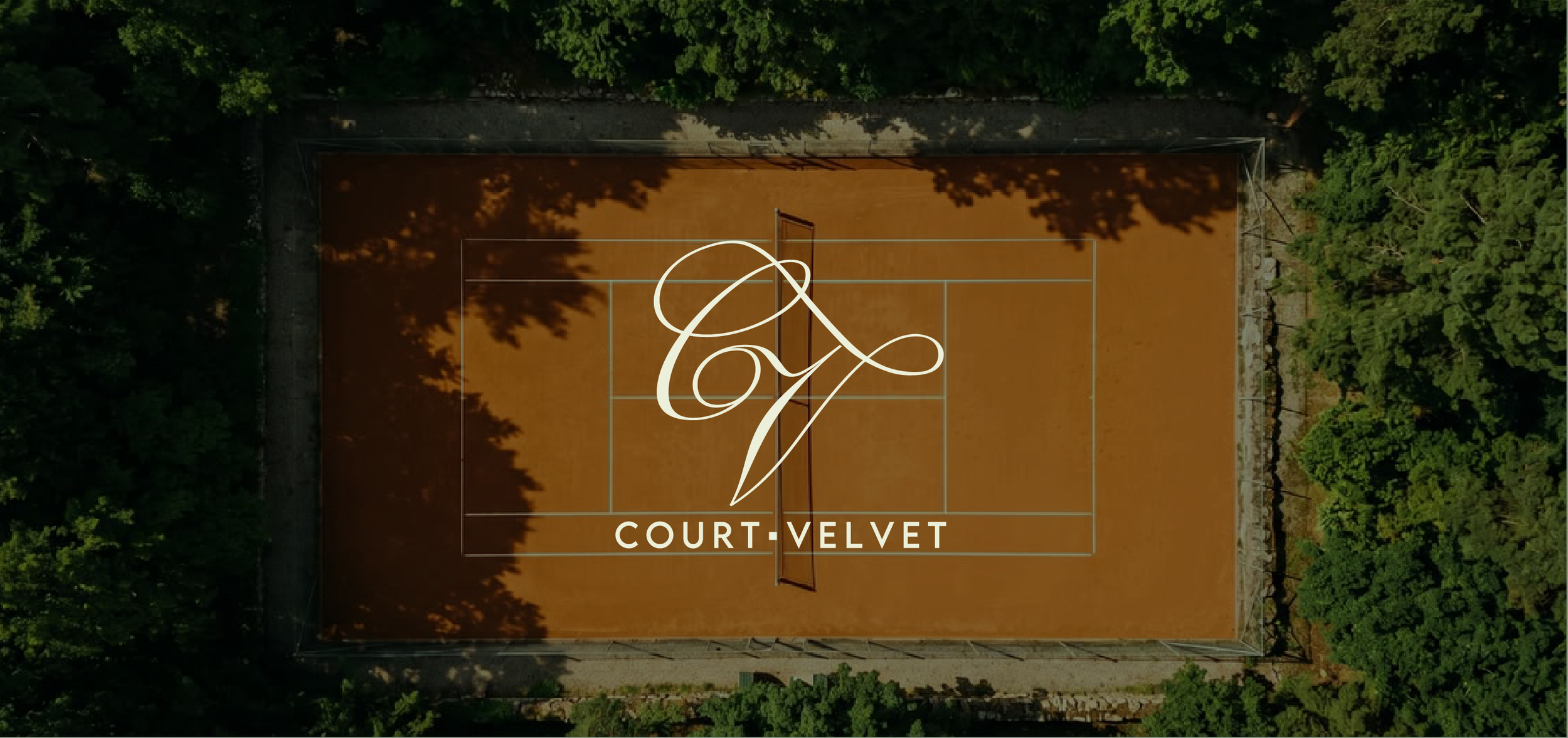 An aerial view of an orange clay tennis court surrounded by green trees. The court features a large white decorative monogram and the text 'COURT VELVET' at the bottom.
