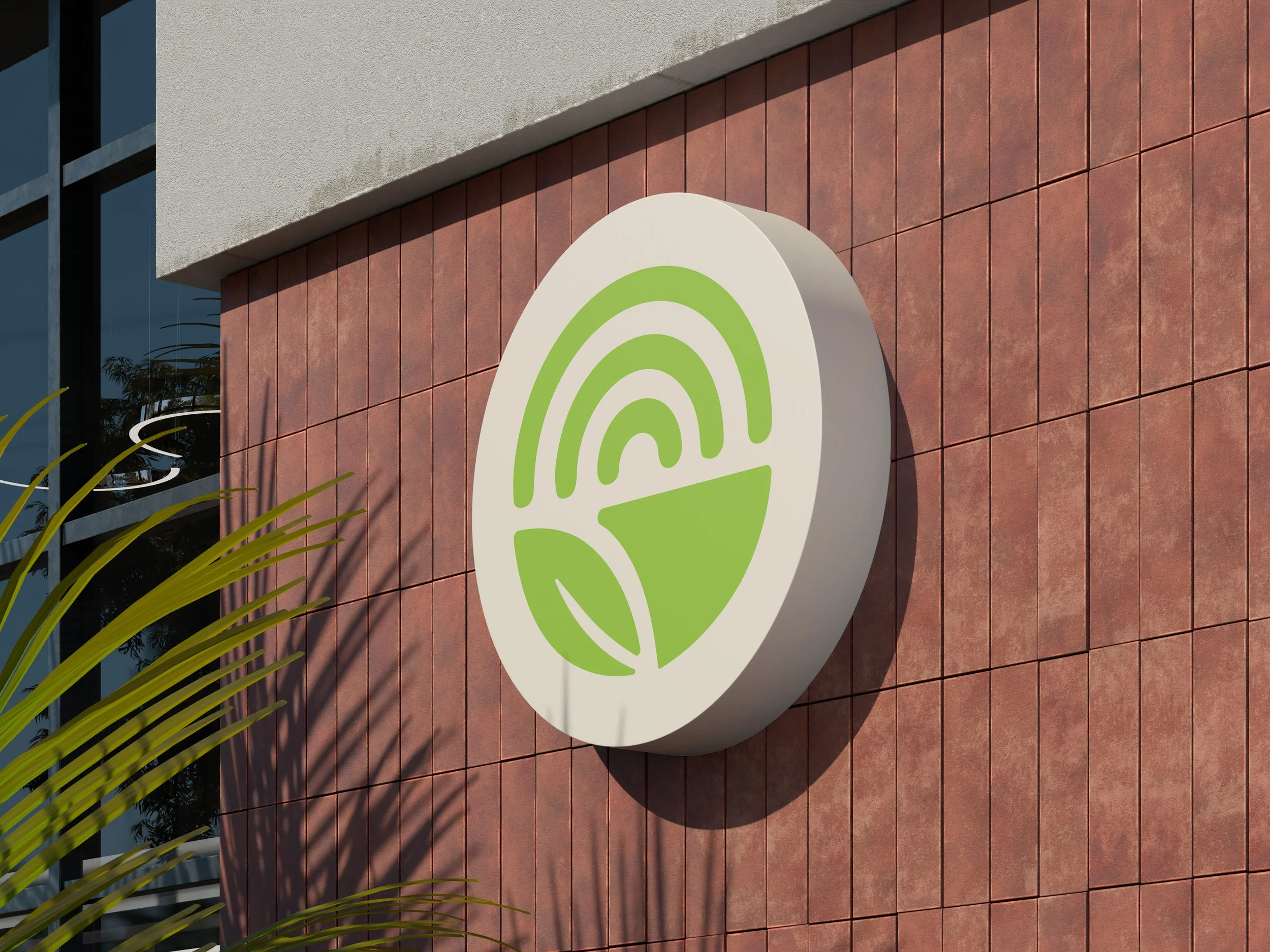A circular sign with green target-like design on a wall with red tiles. Part of a modern building with large windows and plants nearby.