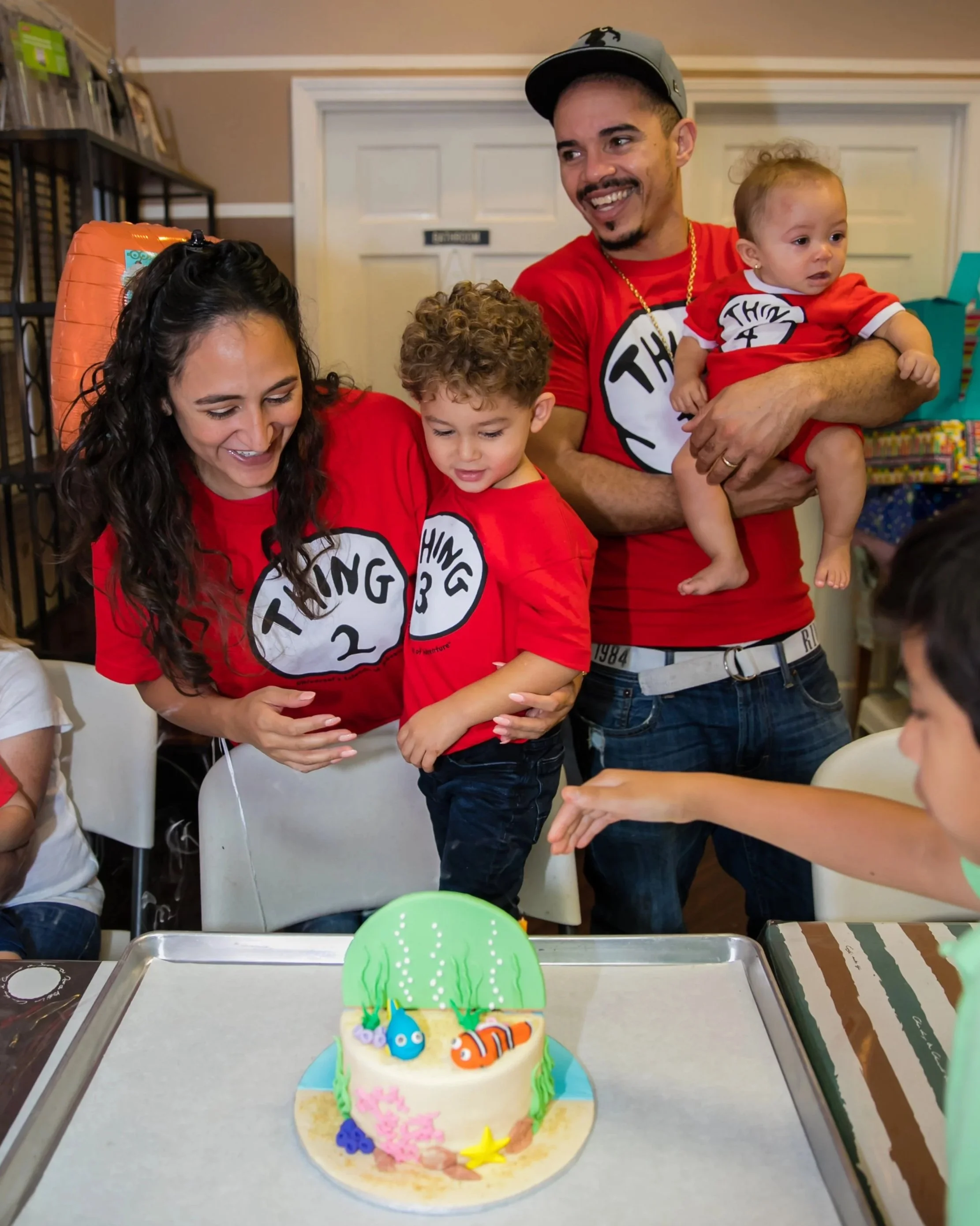 Family celebrating a birthday with a decorated cake featuring ocean-themed decorations,
