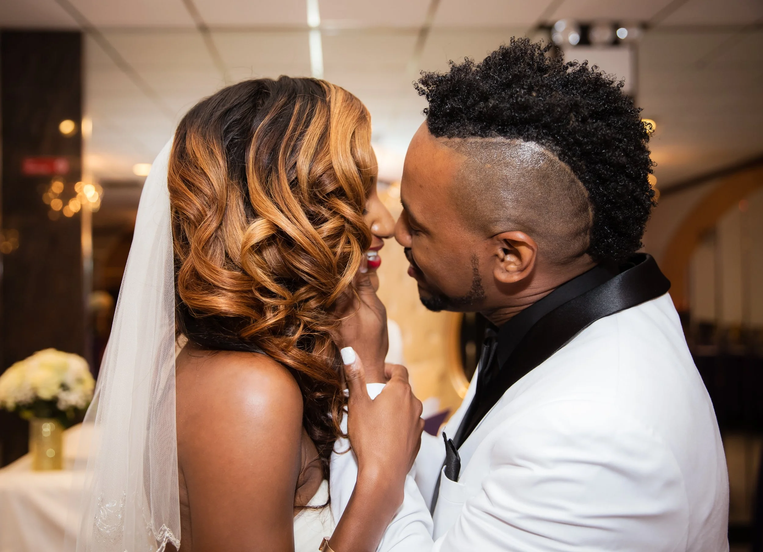 A bride and groom are close face-to-face at their wedding, smiling with their foreheads touching in an intimate moment.
