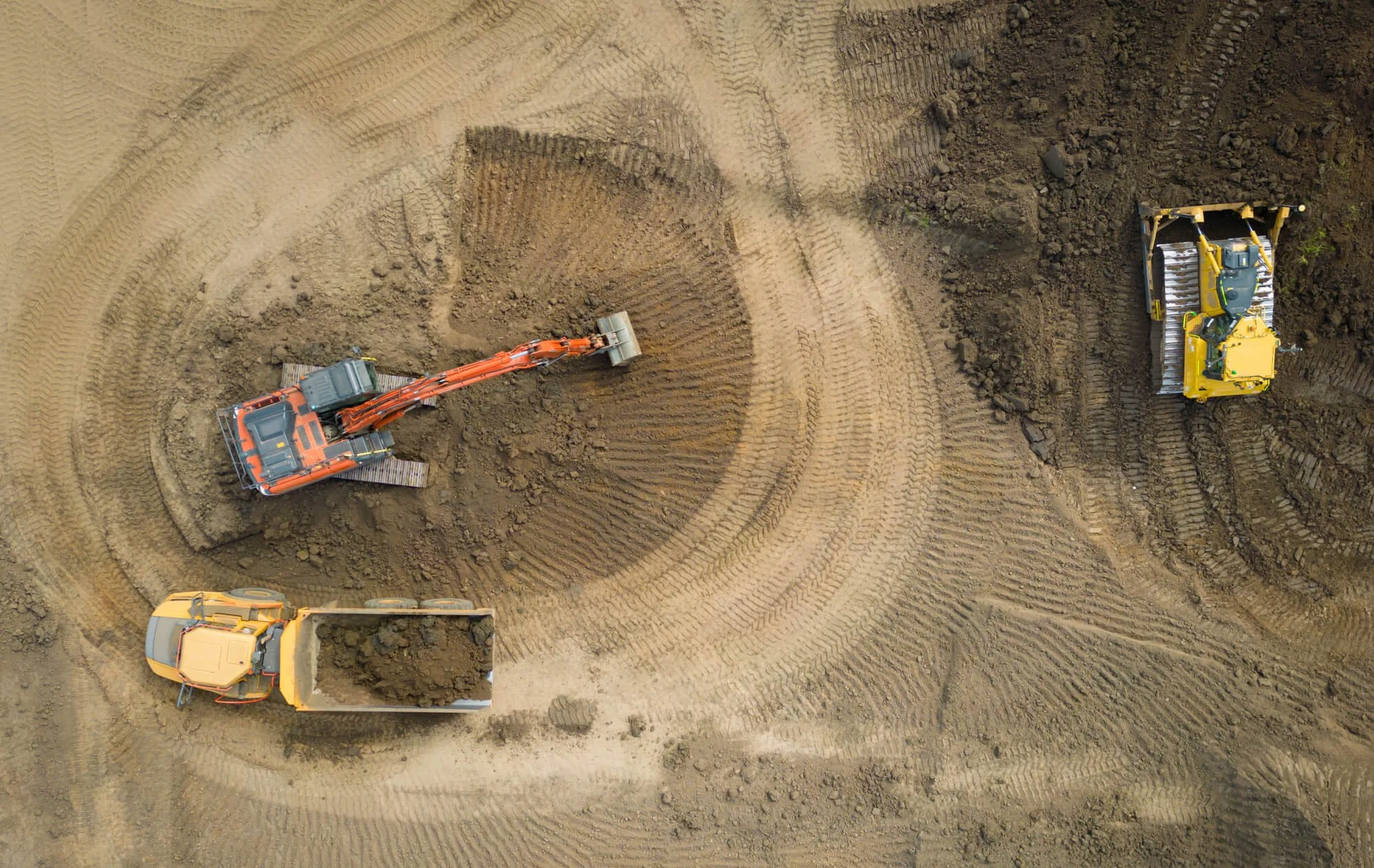 Construction site with earth-moving equipment, including an excavator and a bulldozer, working on leveled soil with visible tire tracks.