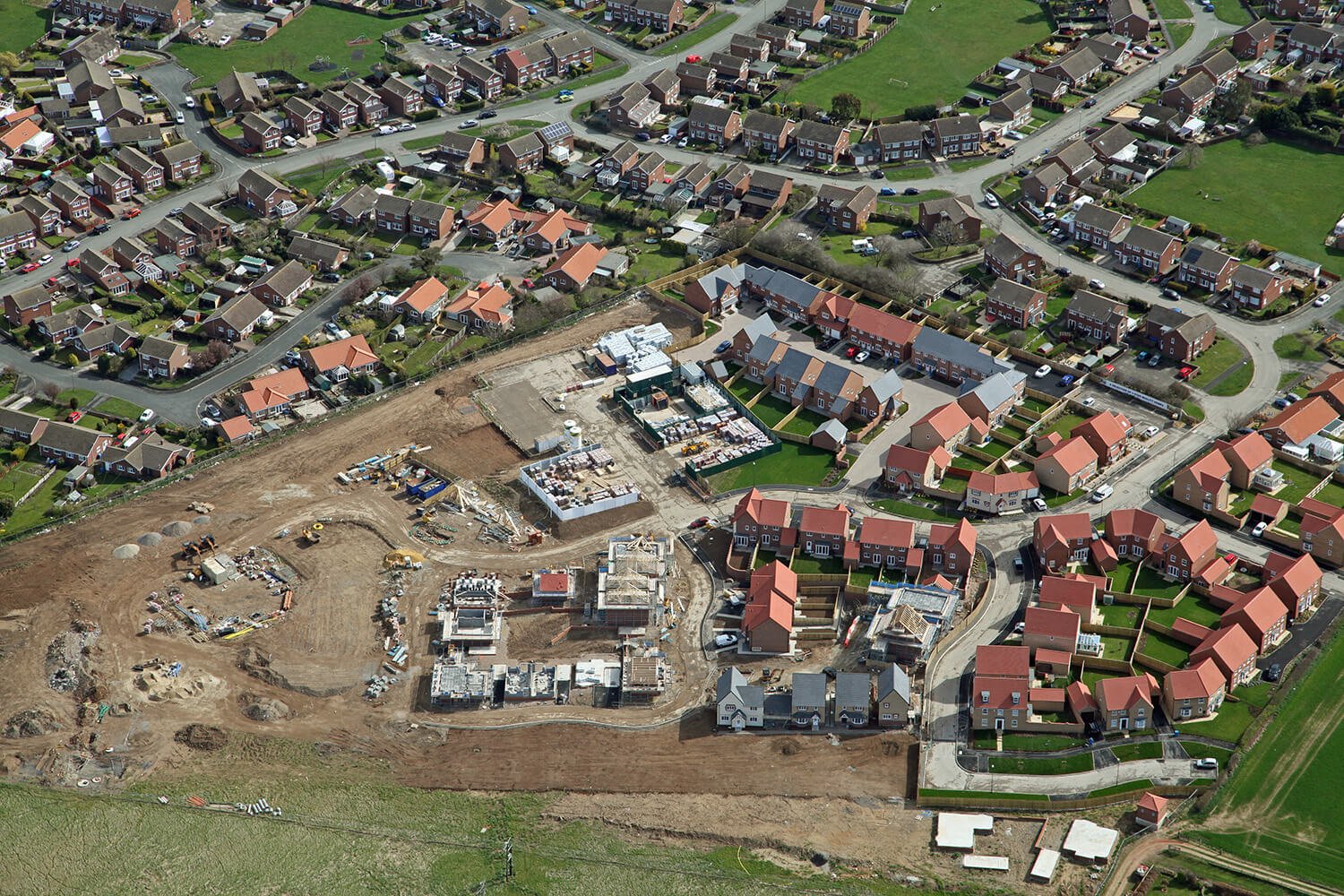 Aerial view of a residential neighborhood with houses, streets, and a construction site with building foundations and equipment.