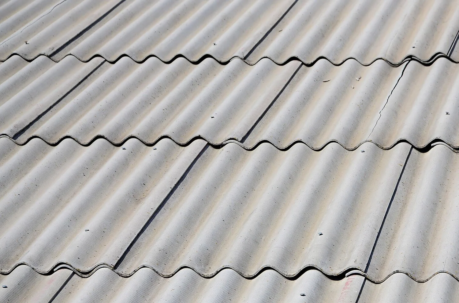 Close-up of a weathered, corrugated metal roof with some visible cracks and dirt.