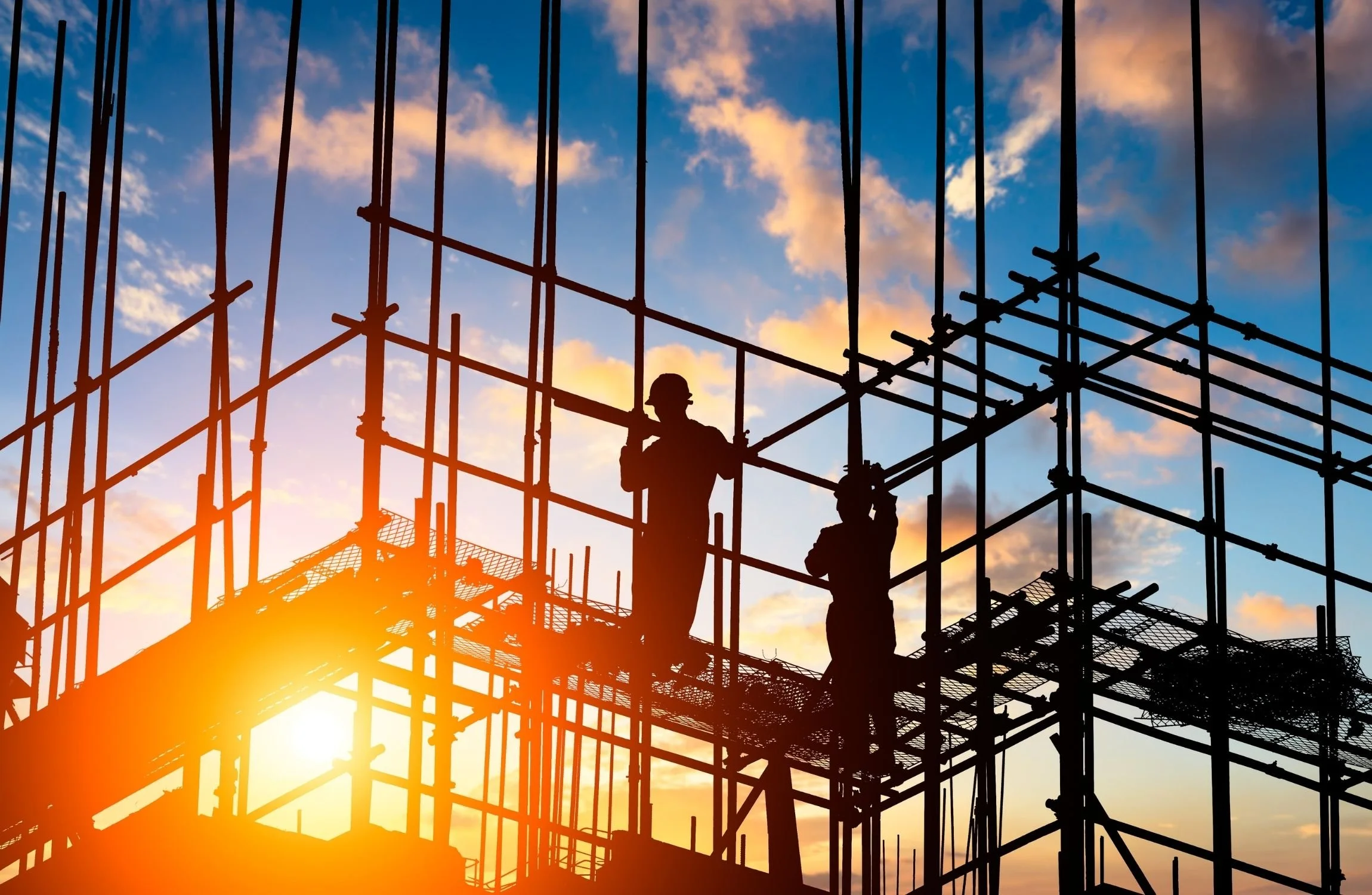 Silhouettes of construction workers on scaffolding against a sunset sky.