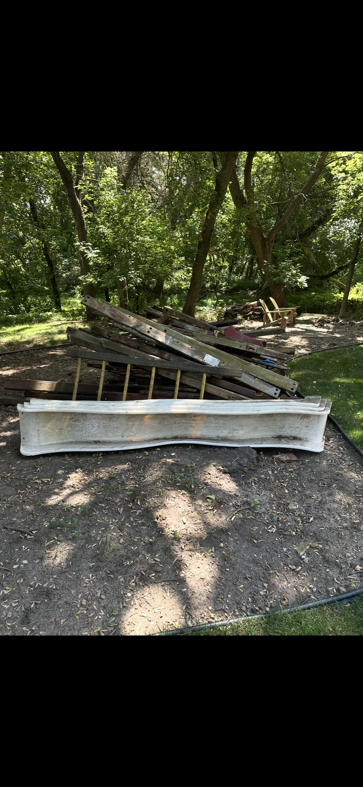 Pile of old wooden garden beds and fencing panels in a backyard with trees and grass.