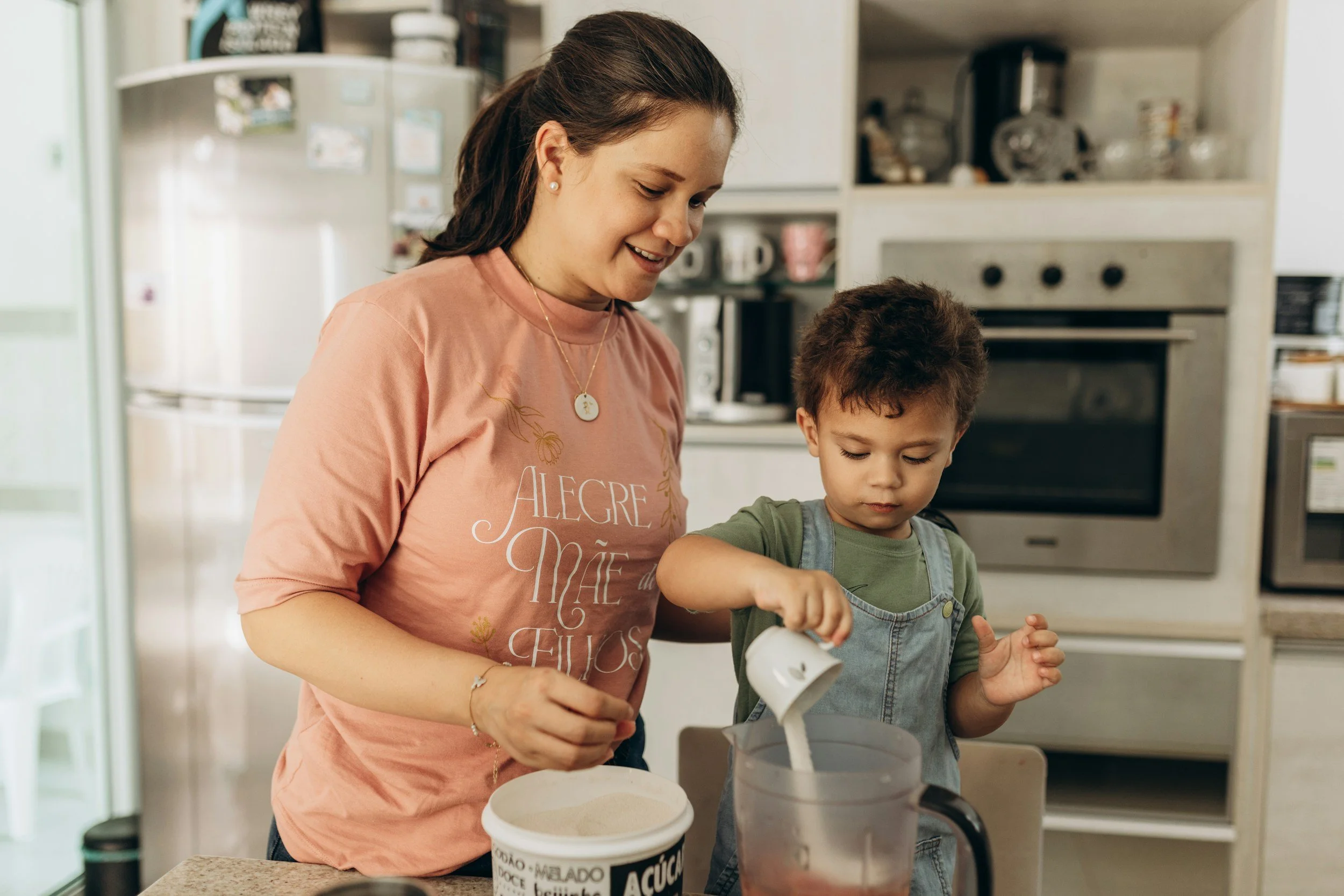 A woman and a young boy, both smiling, preparing ice cream in a kitchen.