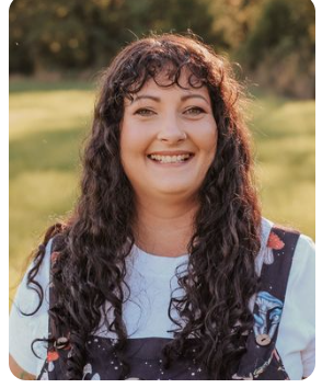Woman with curly dark hair smiling outdoors in a grassy area