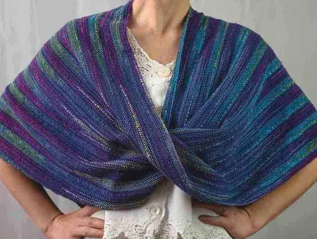 Person wearing a multicolored knitted shawl over a white lace blouse.