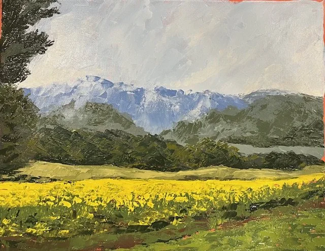 A landscape painting featuring mountains in the background, green hills and trees in the middle ground, and a yellow flowering field in the foreground under a cloudy sky.