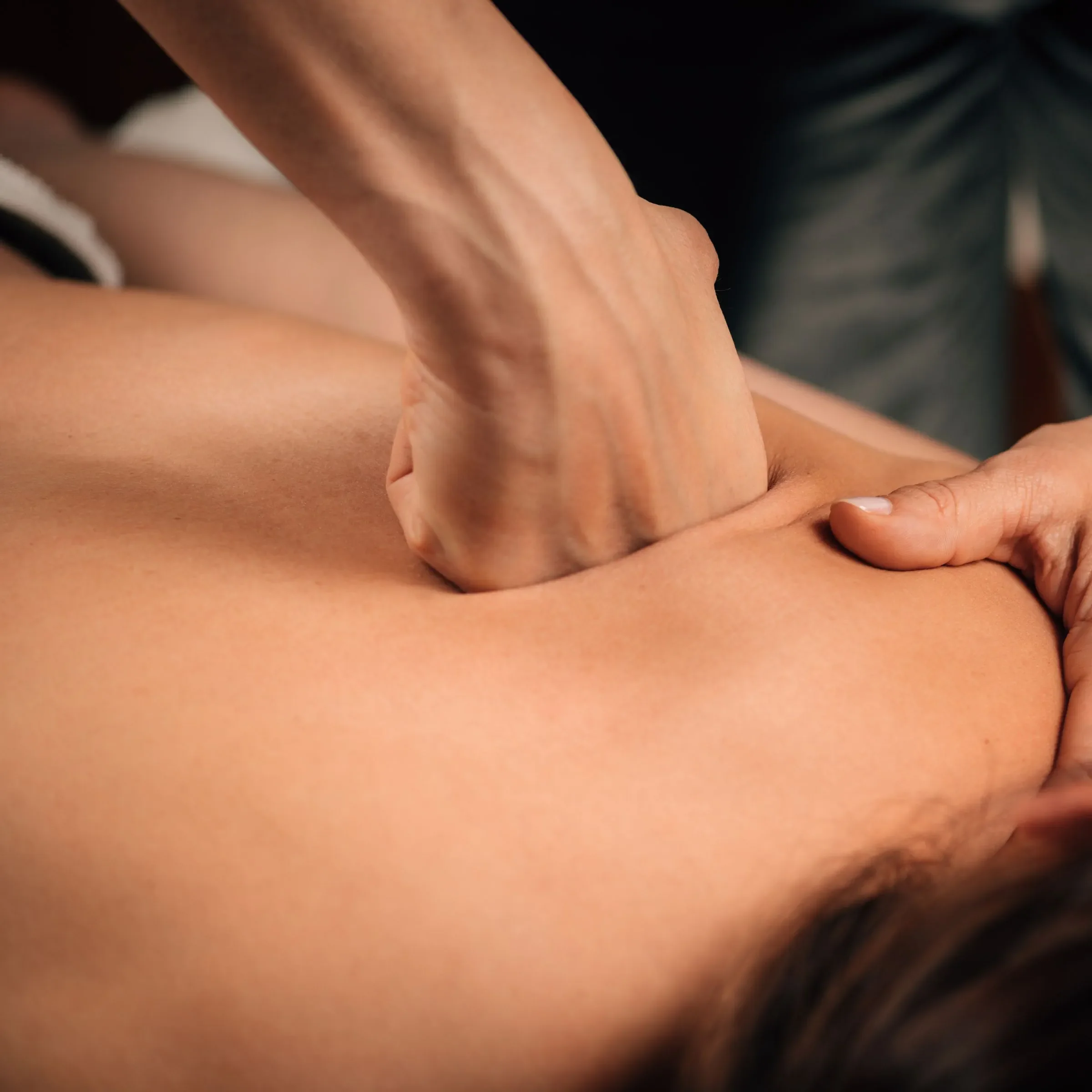 Close-up of a person's firmly pressing on a shoulder, performing Deep Tissue Massage.