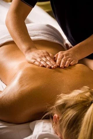 Massage therapist giving a back massage to person lying face down on a table.