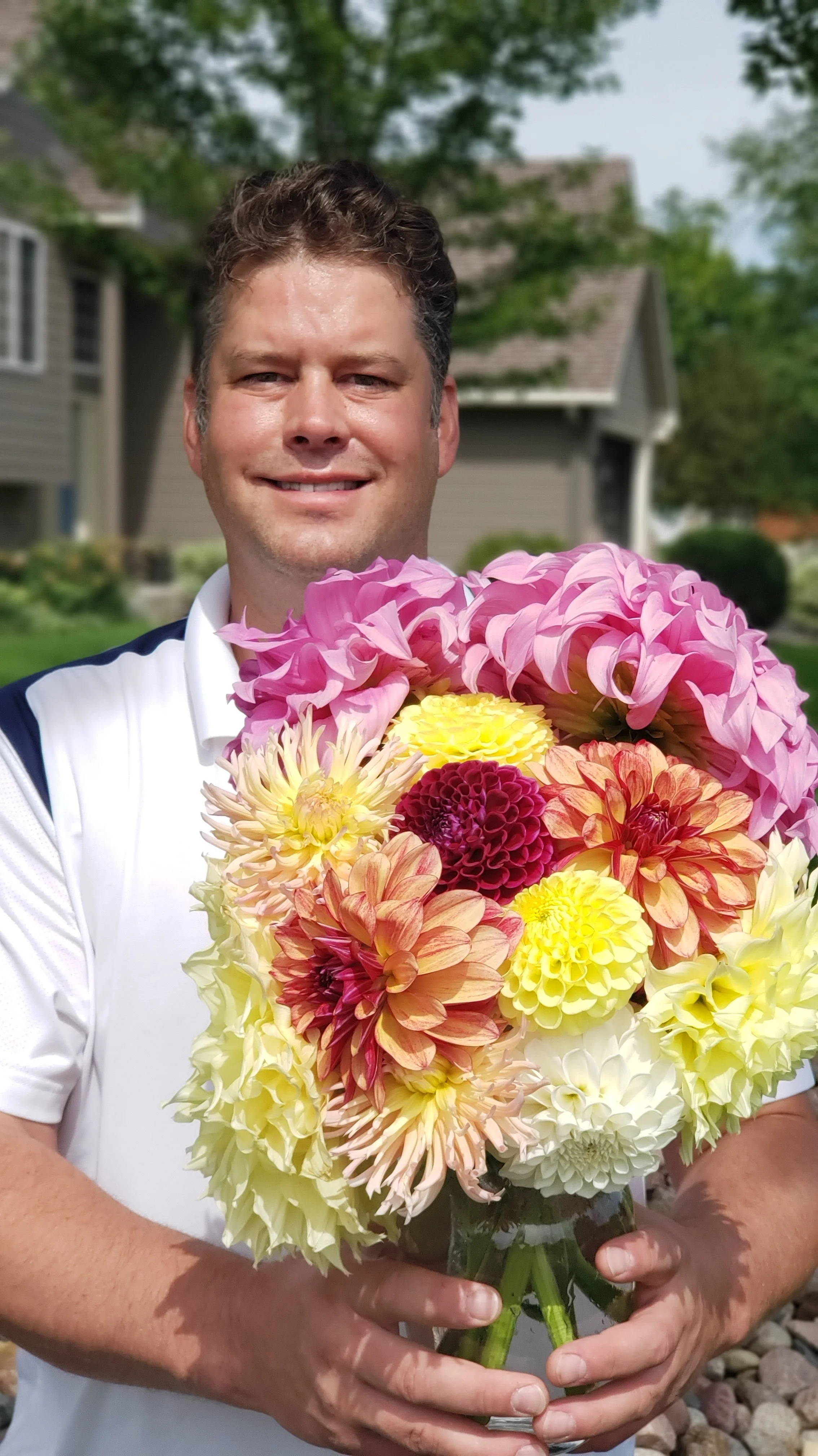 A man holding a colorful bouquet of flowers outdoors with houses and trees in the background.