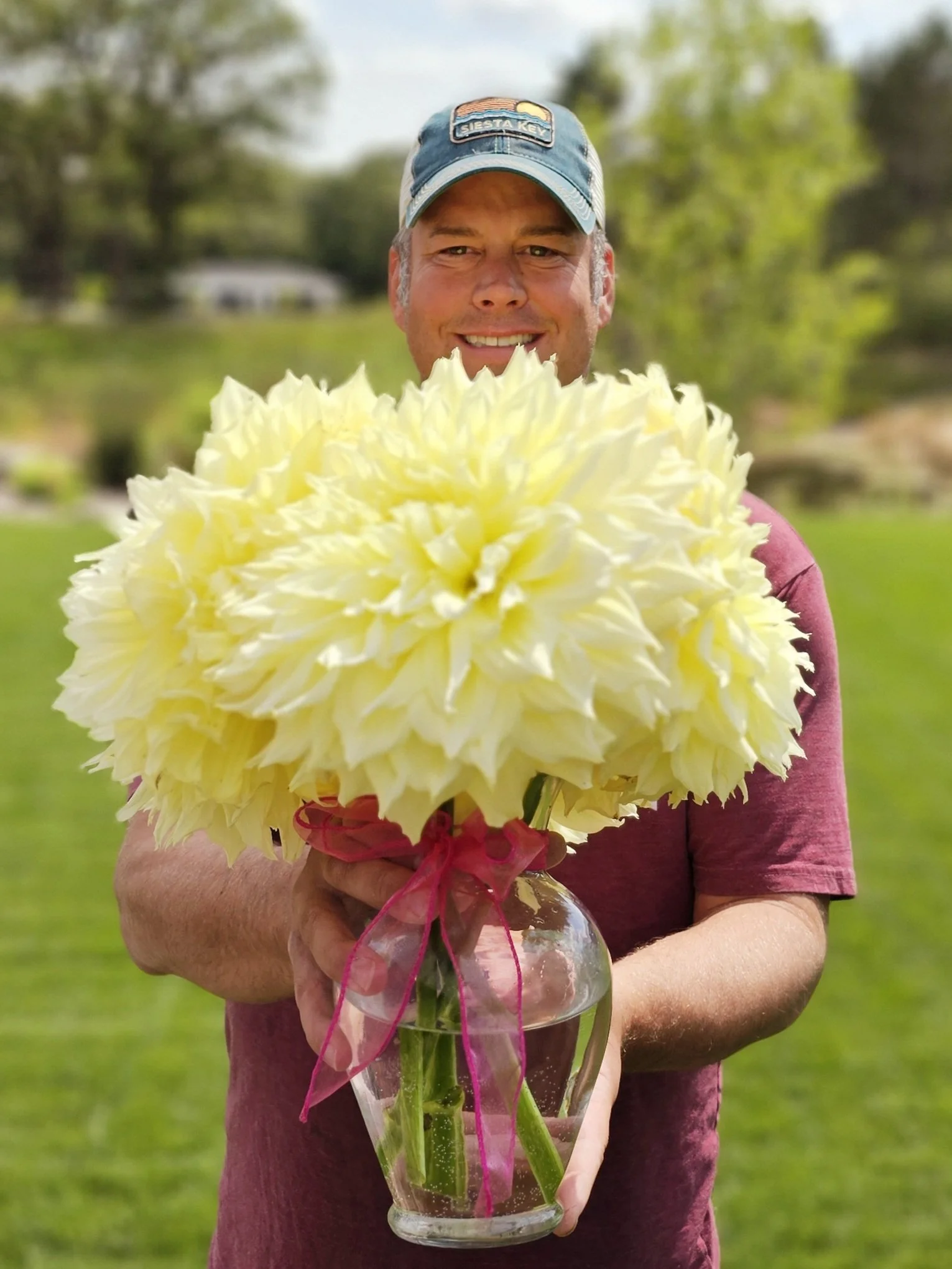 Person holding a large yellow flower arrangement in a glass vase outdoors.