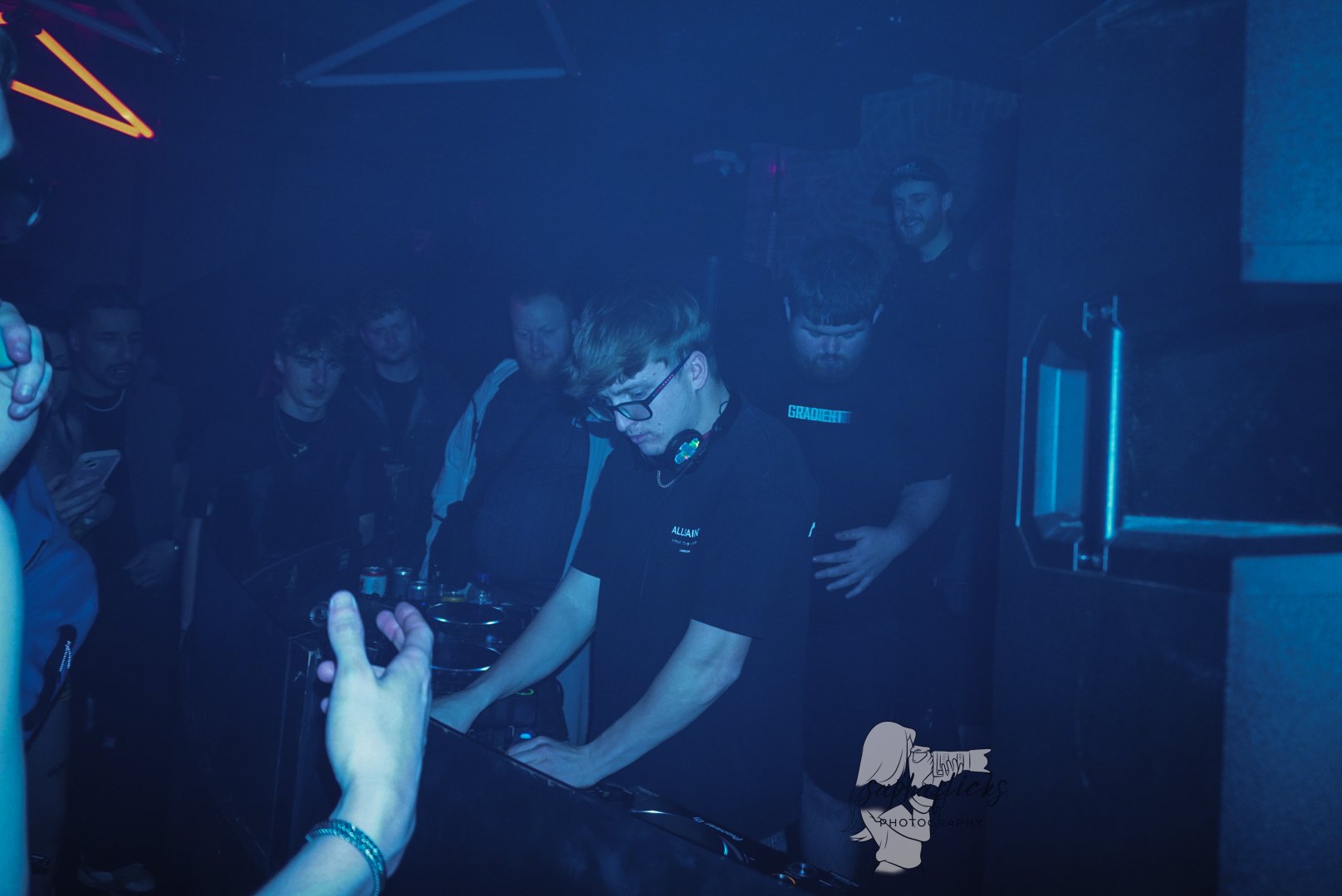 DJ performing at a nightclub with a crowd of people watching, illuminated by blue lighting.