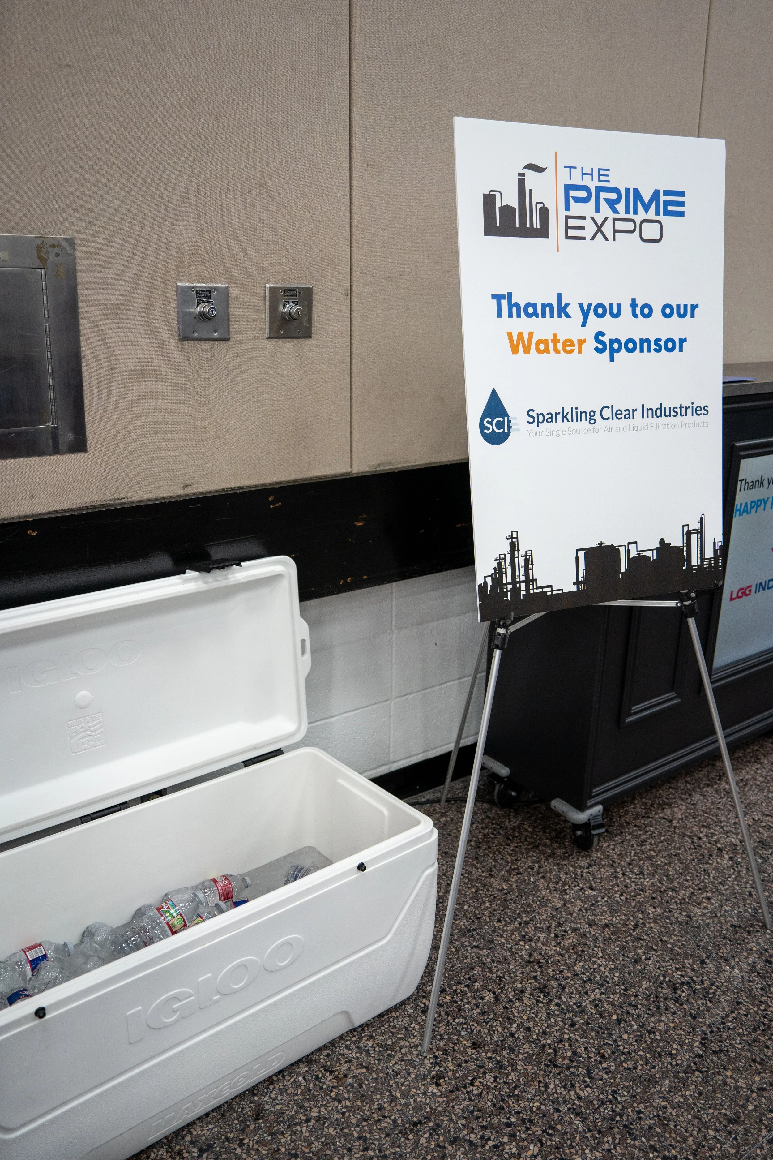 A sign at a conference thanking Sparkling Clear Industries as the water sponsor, with a cooler filled with bottled water in front.
