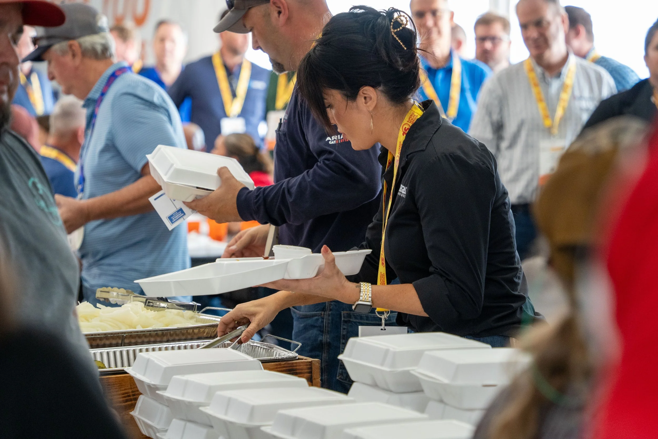 People are serving themselves food at a buffet, with white foam food containers, at a gathering or event.
