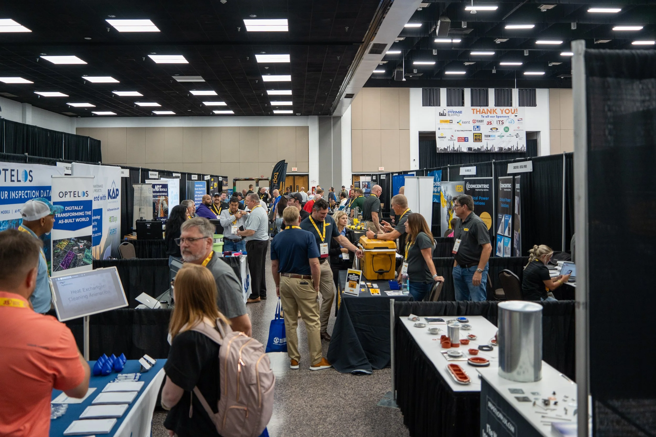 A busy convention center hall filled with various exhibition booths and attendees networking and exploring displays.