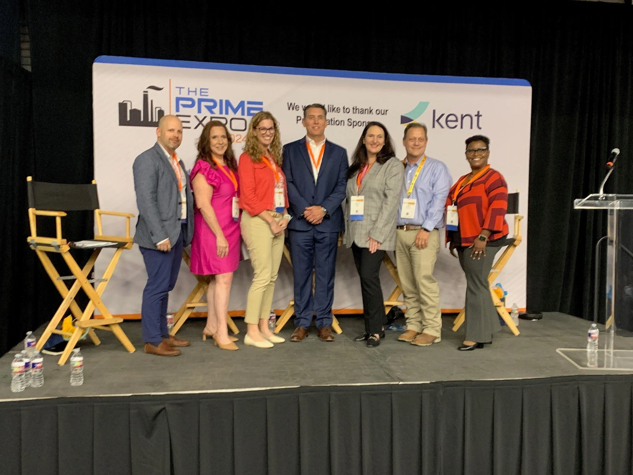 Group of seven people standing on stage at a conference, with a panel backdrop displaying 'The Prime Expo 2023' and 'Kent' logo, some holding name badges.