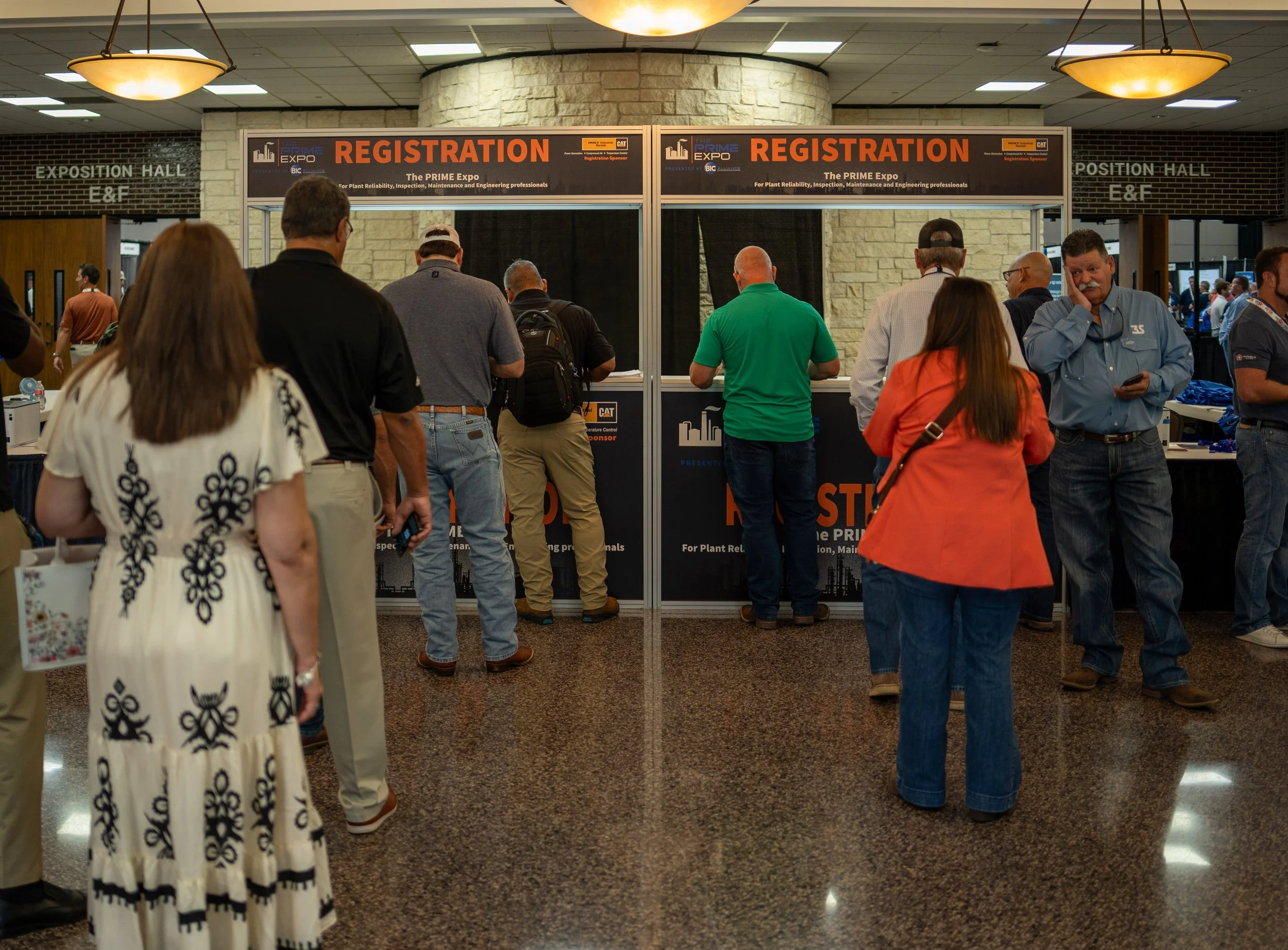 People standing in line at a registration booth at a conference or trade show, with signs labeled 'Registration' and 'The PRIME Expo' in the background.