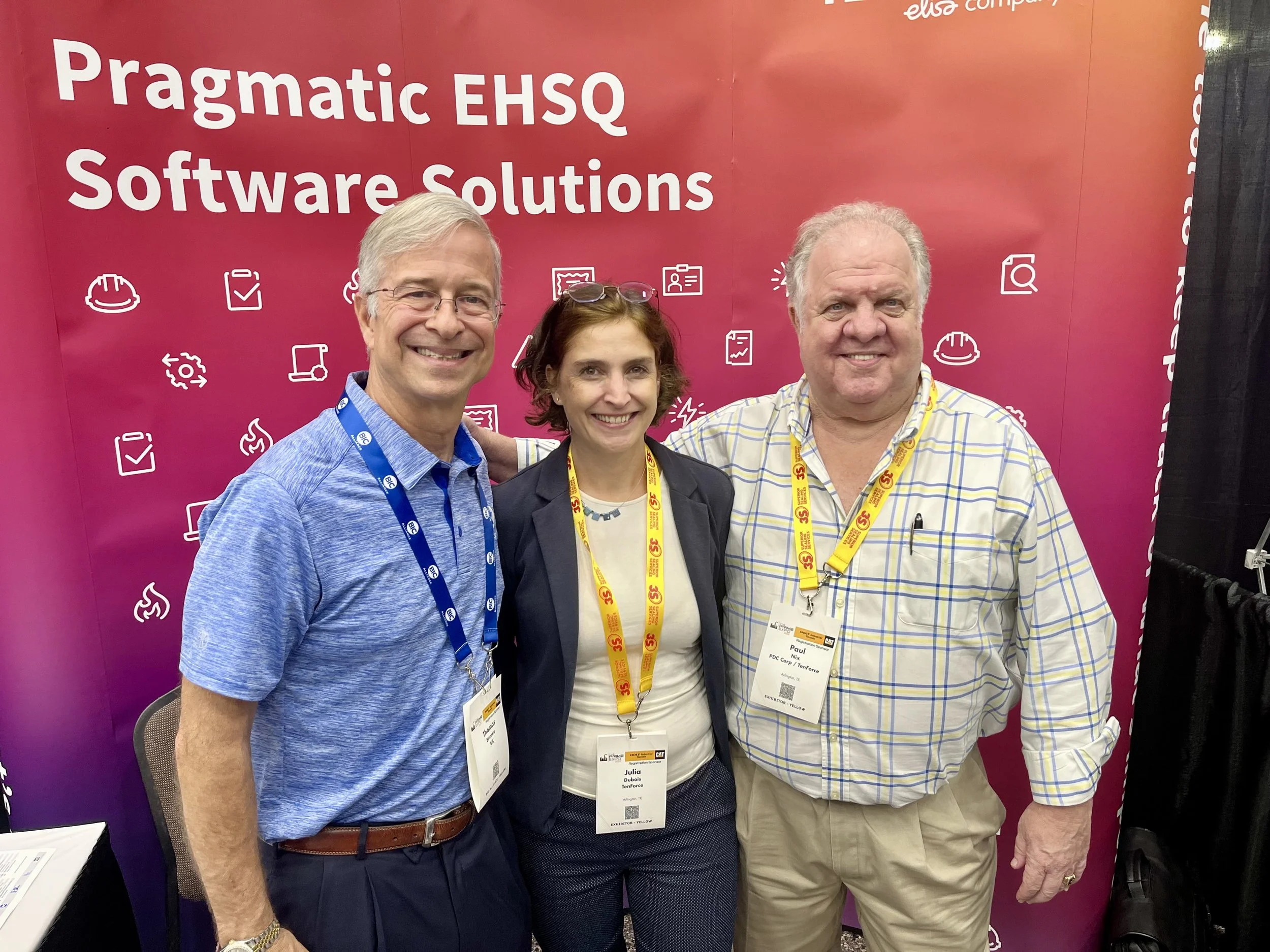 Three people standing in front of a red backdrop with white text and icons at the Pragmatic EHSQ Software Solutions conference. They are smiling and wearing conference badges and lanyards.