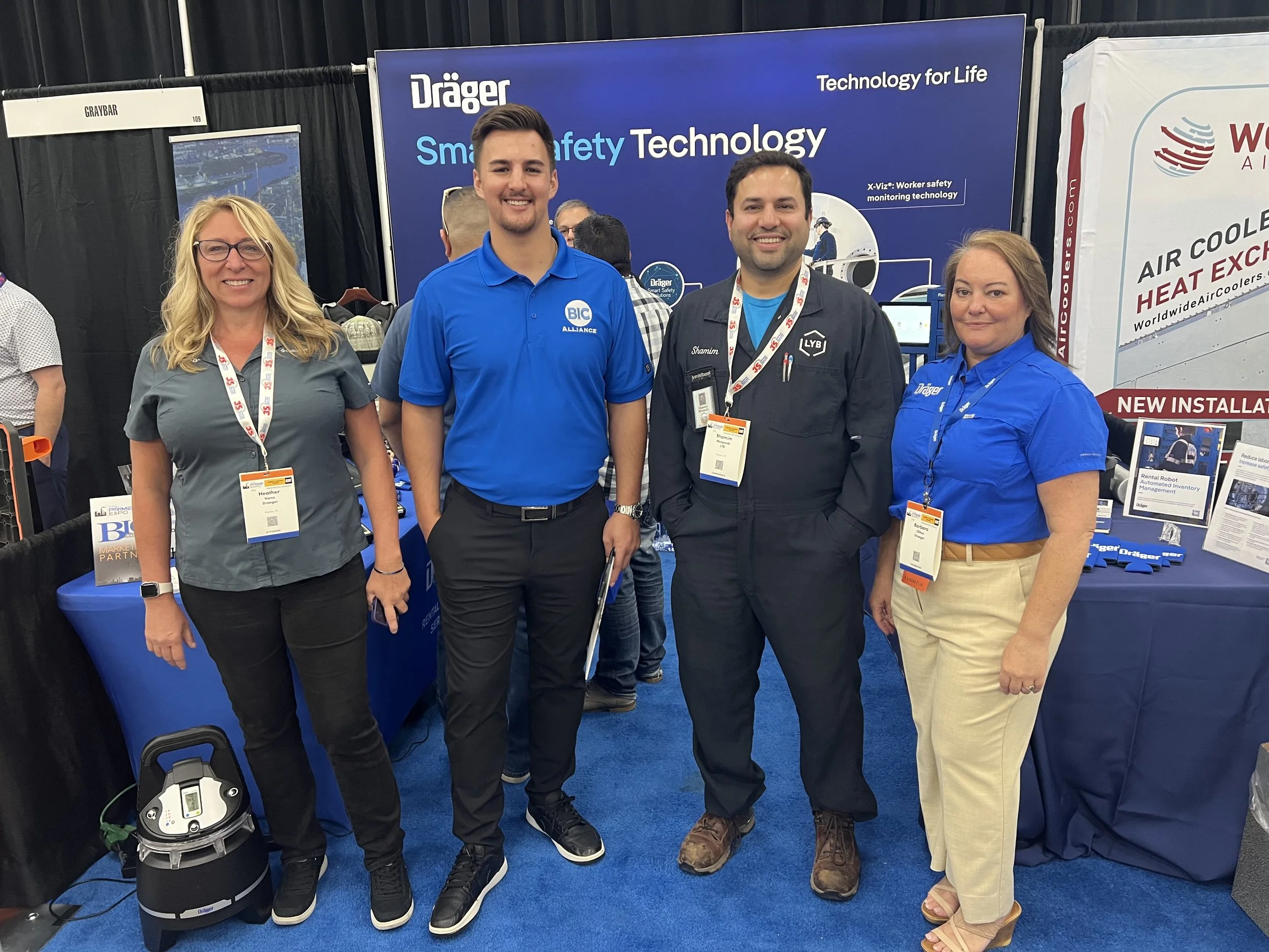 Four smiling people standing in front of a booth at a trade show, with banners displaying 'Dräger' and 'Smart Safety Technology' in the background.