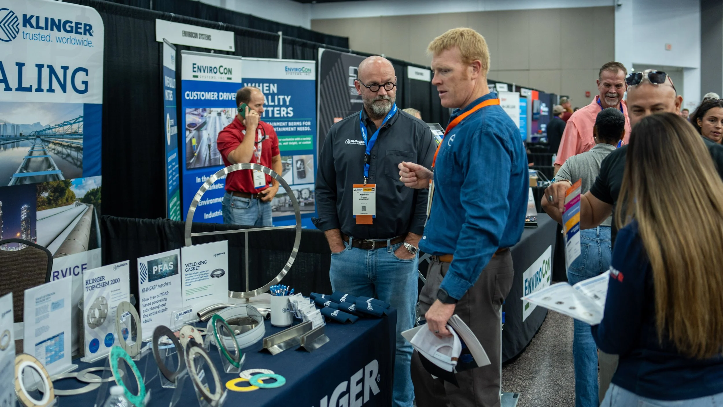 People at an industry trade show or conference, with displays and promotional materials for Klinger and EnviroCon.