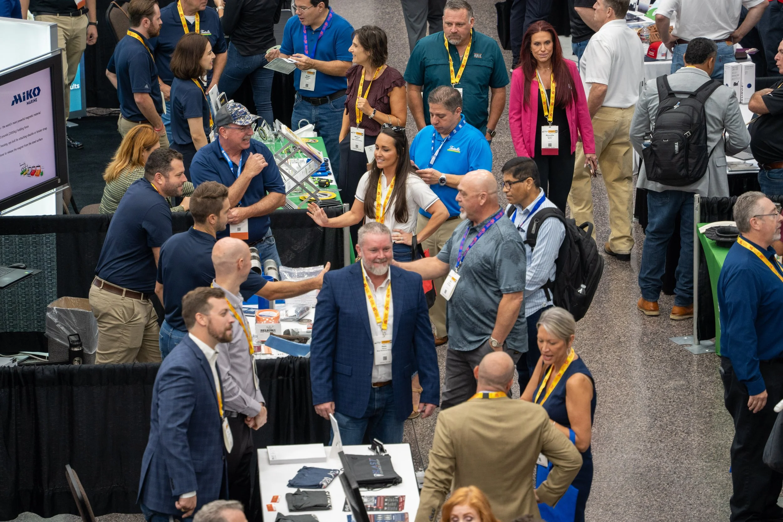 People talking and networking at a trade show or conference, with booths and displays visible.