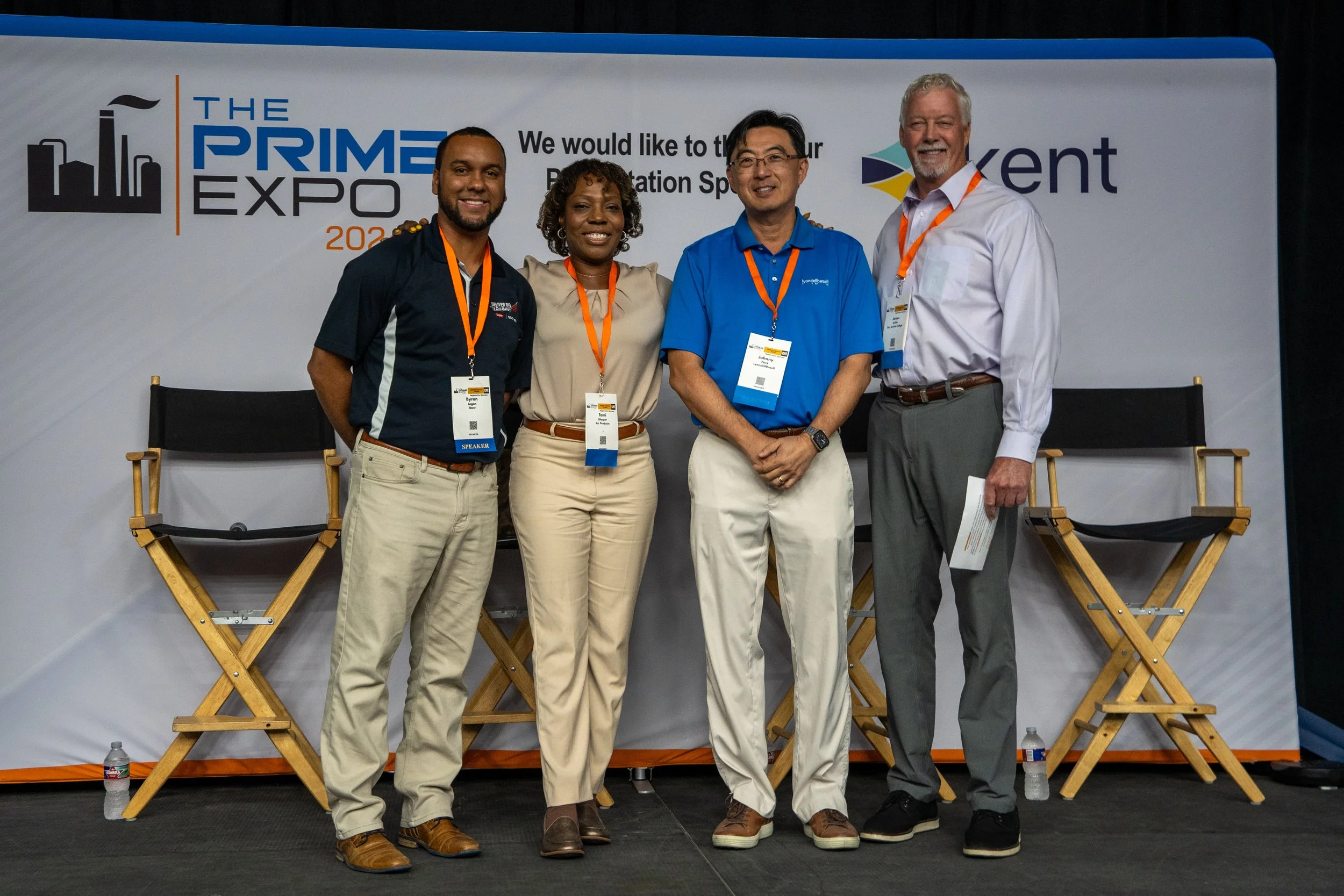 Four individuals standing on a stage at The Prime Expo 2023, smiling for a photo. They are wearing conference badges with orange lanyards. Behind them is a backdrop with the event's logo and the word 'Xent' visible.