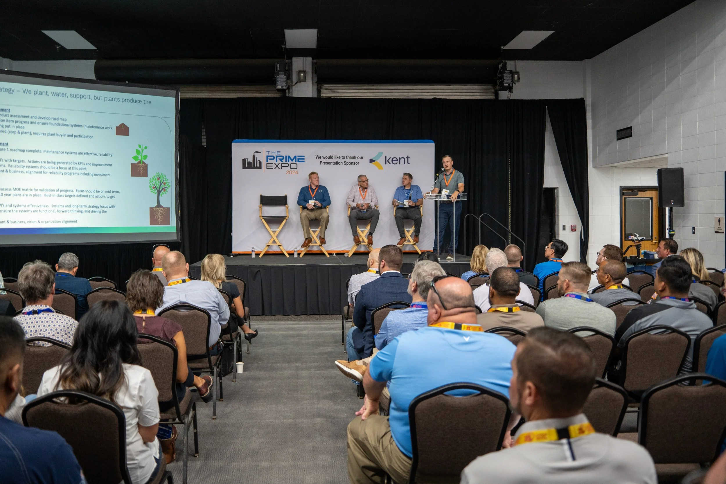 A conference scene with a speaker at a podium on stage, four panelists seated in chairs, and an audience listening. Large screen displays a presentation slide, event banners read 'The Prime Expo 2024' and sponsor 'Kent.'