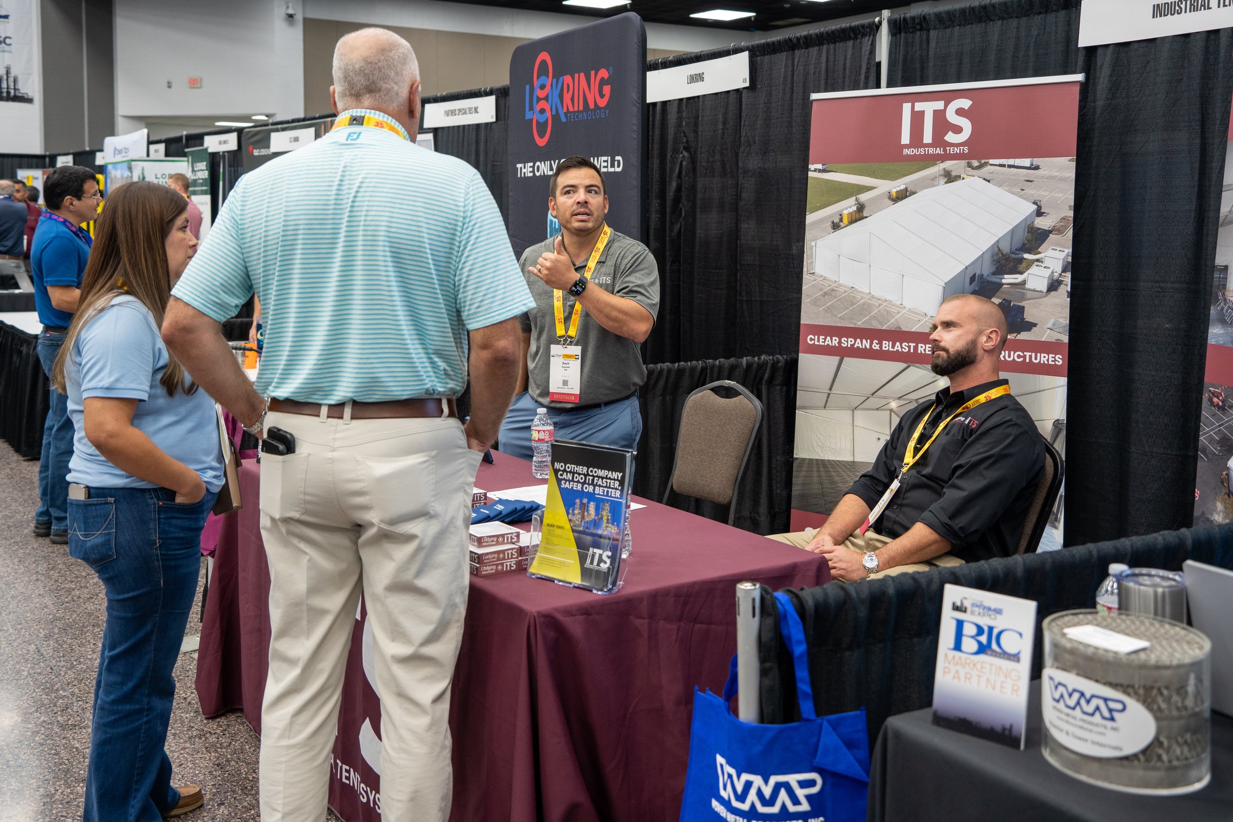 At a trade show booth, a man and a woman are talking to two exhibitors behind a table, with banners for ITS industrial tents and LKring technology in the background.