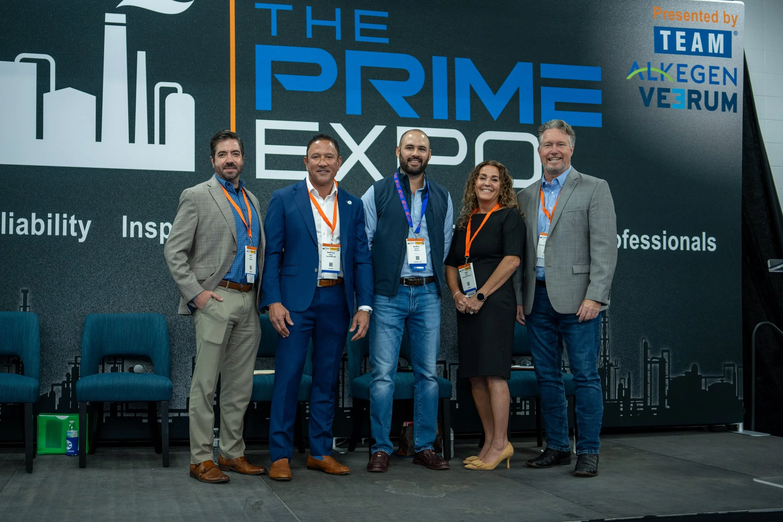 A group of six professionally dressed people standing in front of a large sign at a conference or expo, smiling for the camera.