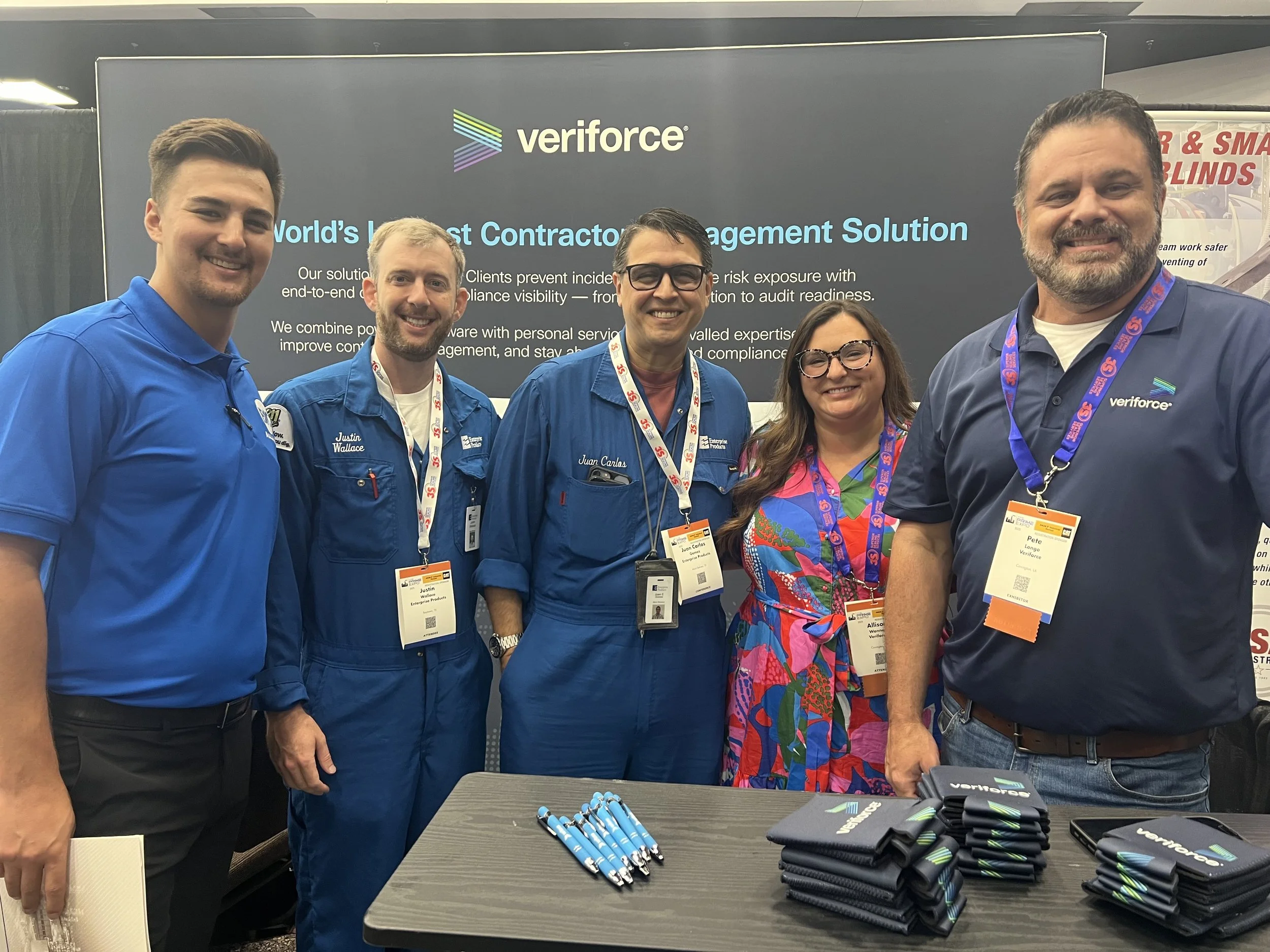 Five people standing in front of a Veriforce display at a conference, smiling, with pens and branded items on the table.