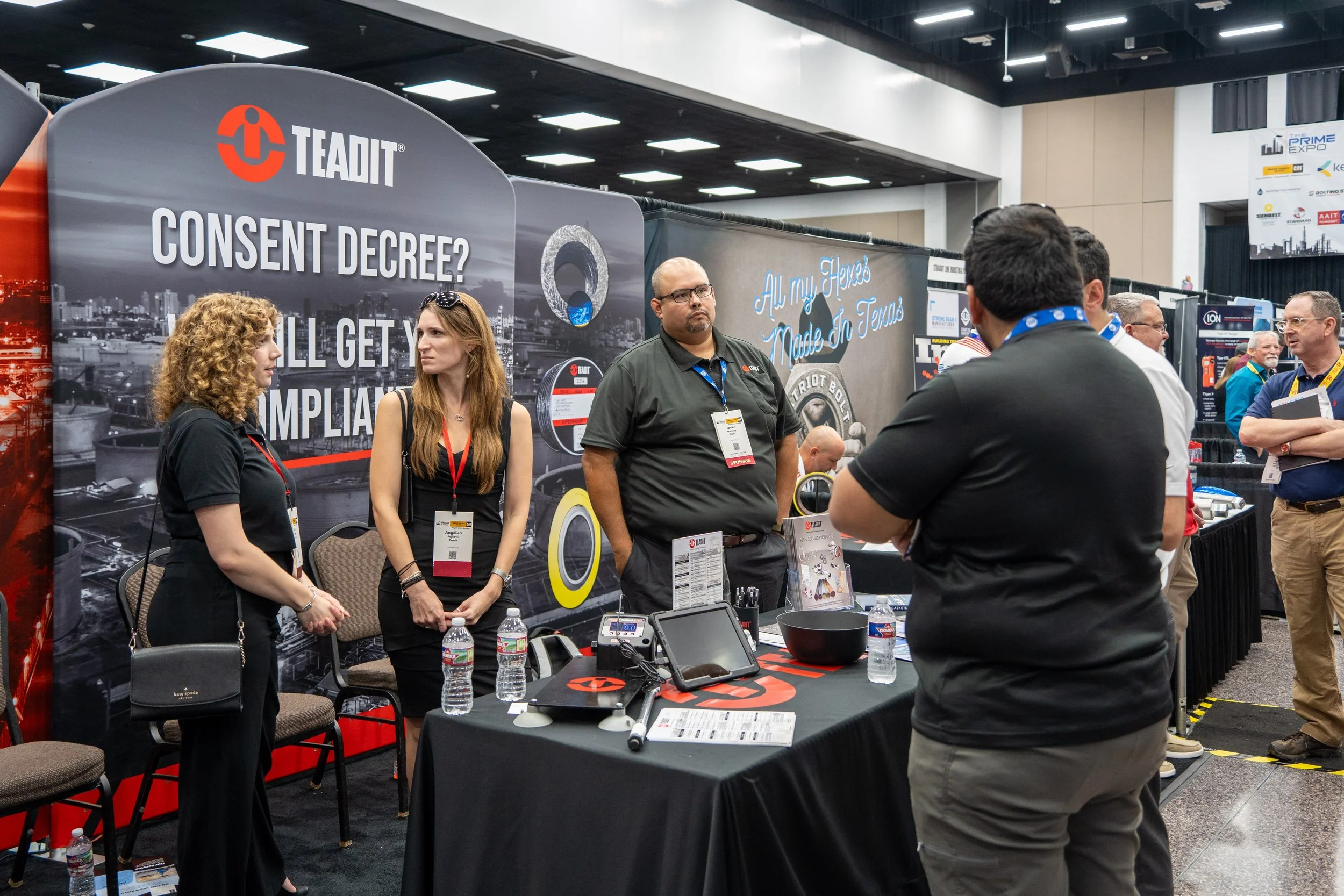 Trade show booth for TEADIT featuring a large banner with the text "Consent Decree? You’ll Get Violations" and attendees engaging in conversation