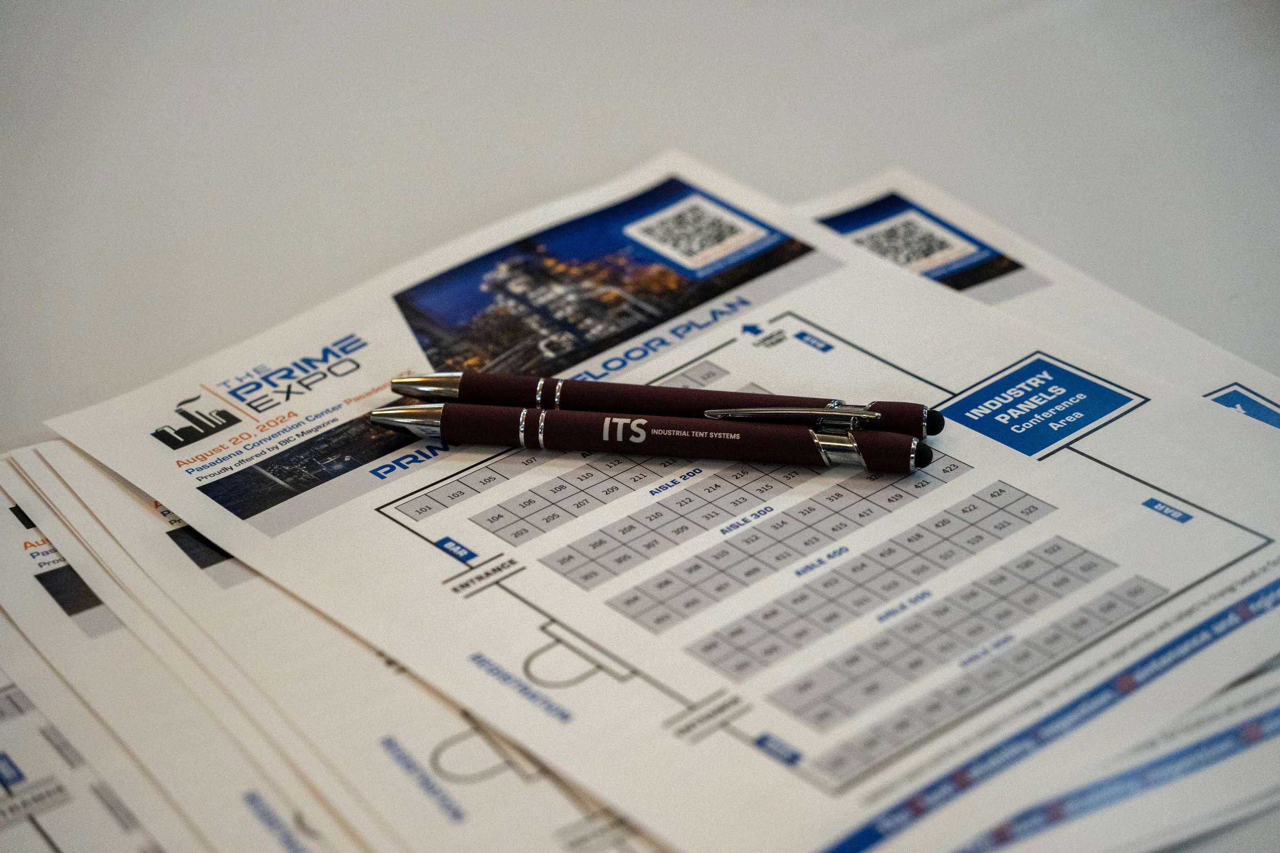 Conference brochures and pens on a table at a trade event.