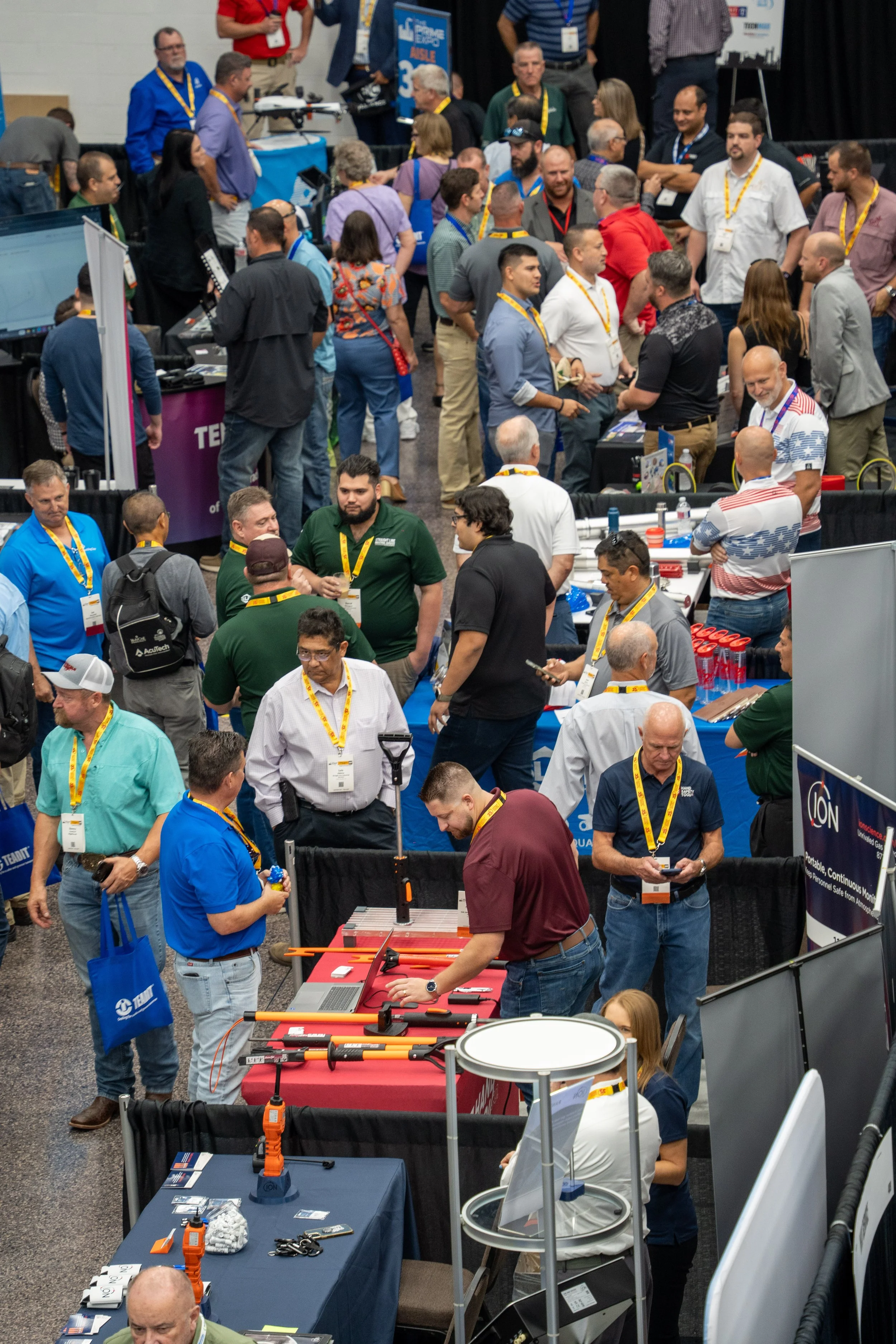A crowded trade show or conference with many attendees browsing booths and displays in a large hall.