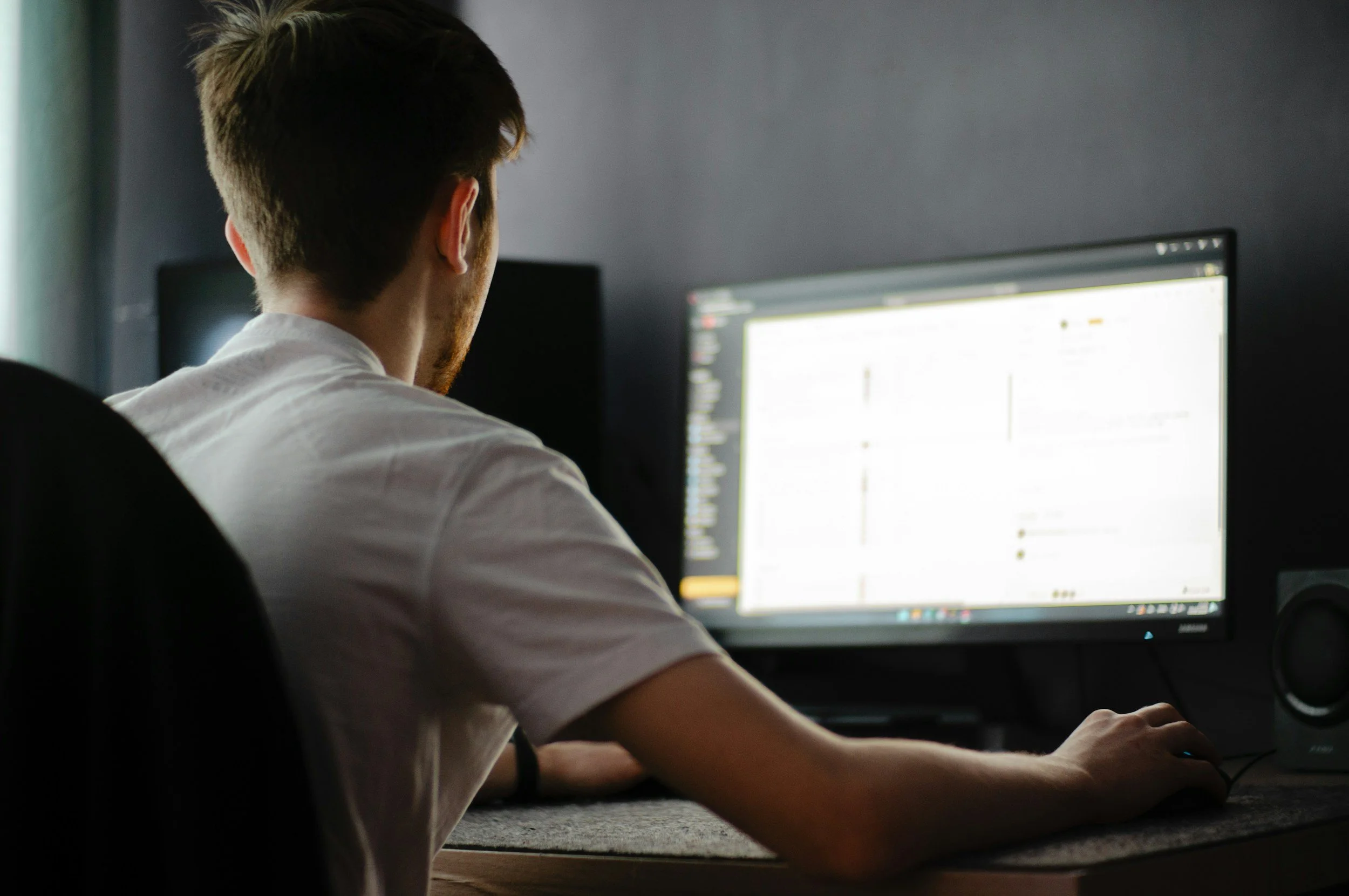A person sitting at a desk working on a computer in a dimly lit room.
