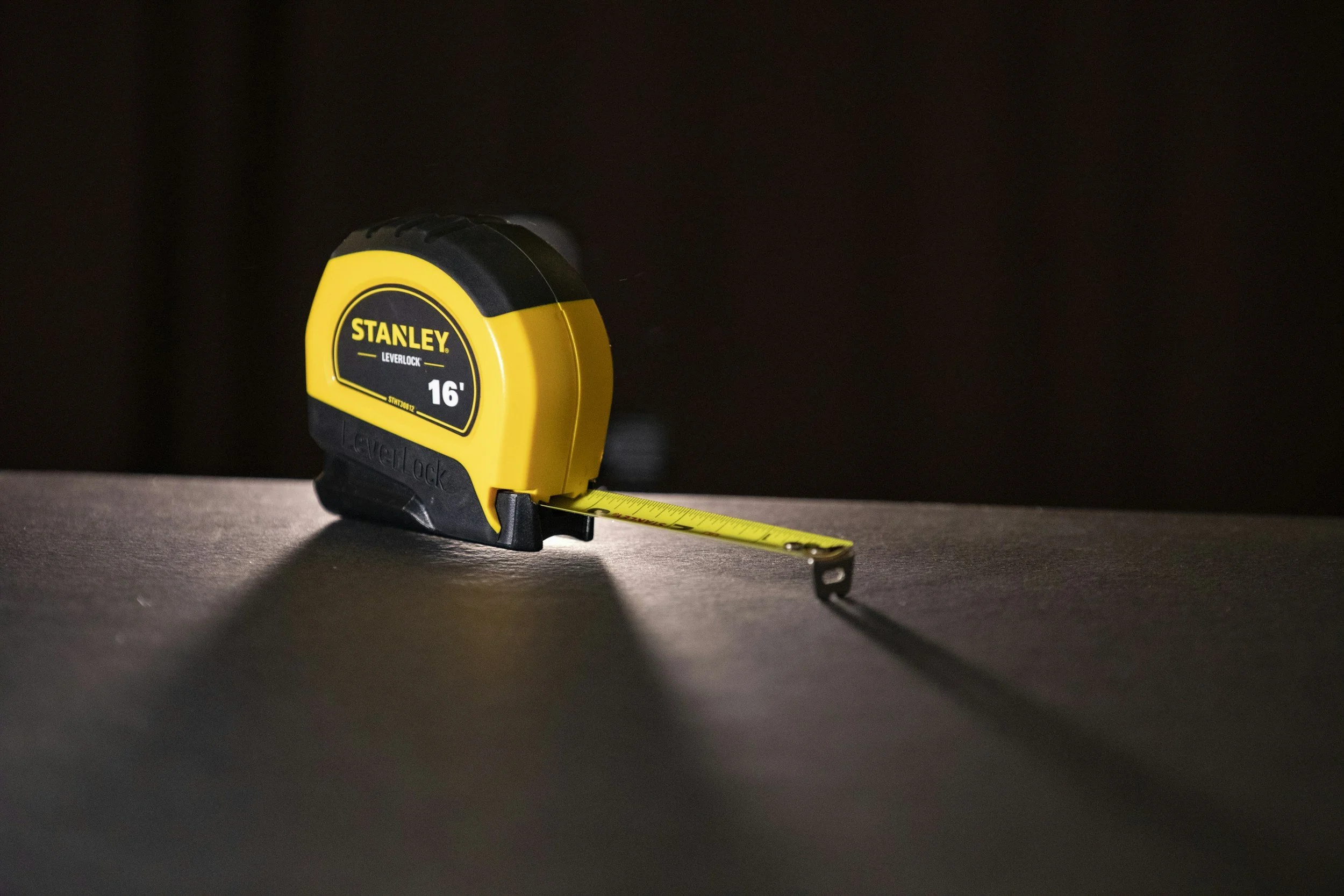 Yellow and black Stanley tape measure extended on a dark surface.