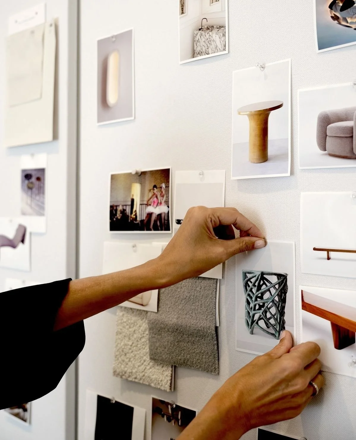 Person pinning a photograph of decorative objects on a white display board with other images and fabric swatches.